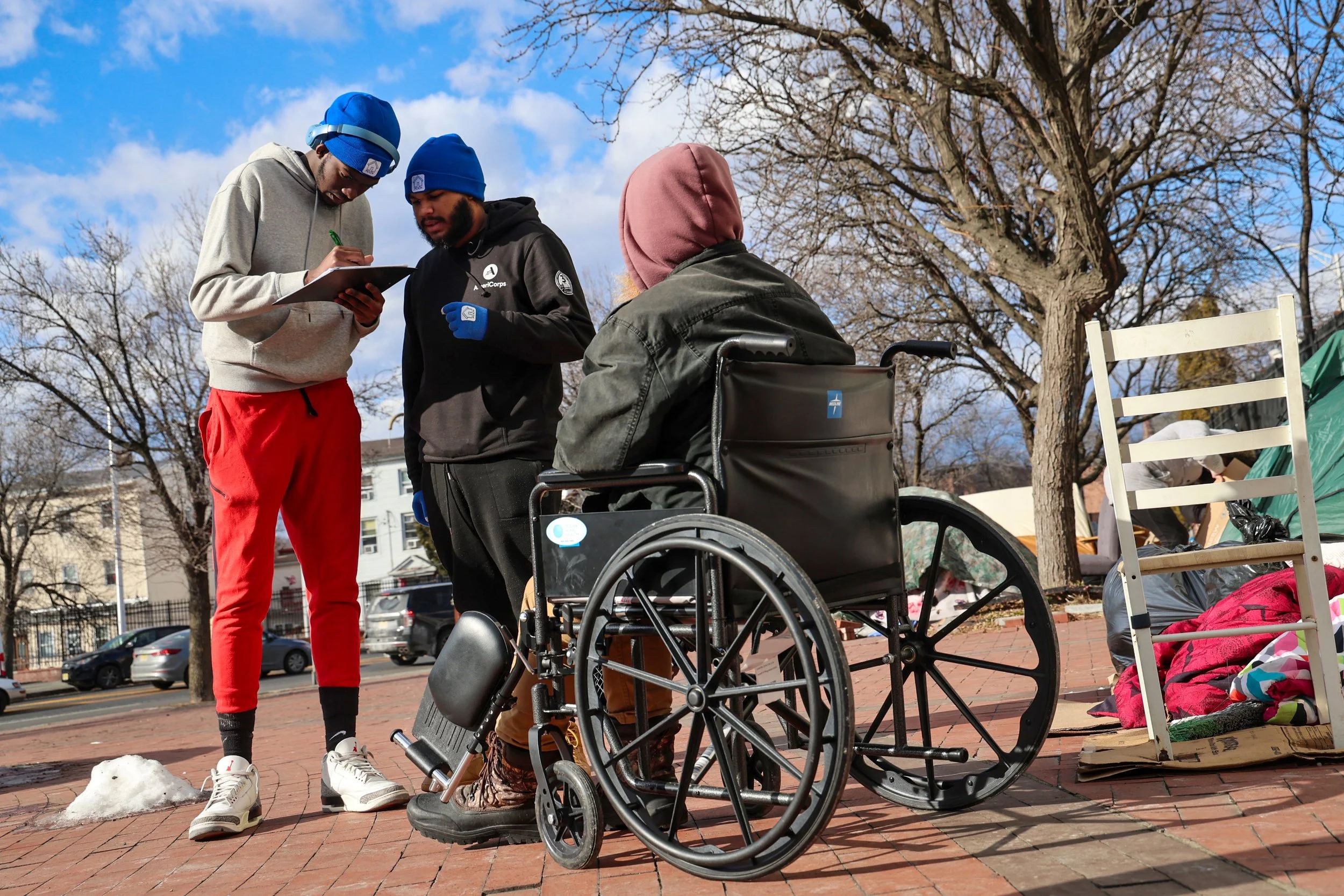 PATERSON, N.J. | 01-29-2025 — POINT-IN-TIME SURVEY: AmeriCorps members collect information from a homeless individual in a wheelchair at a homeless encampment off a highway exit ramp while conducting the annual Point-in-Time (PIT) Count, a nationwide