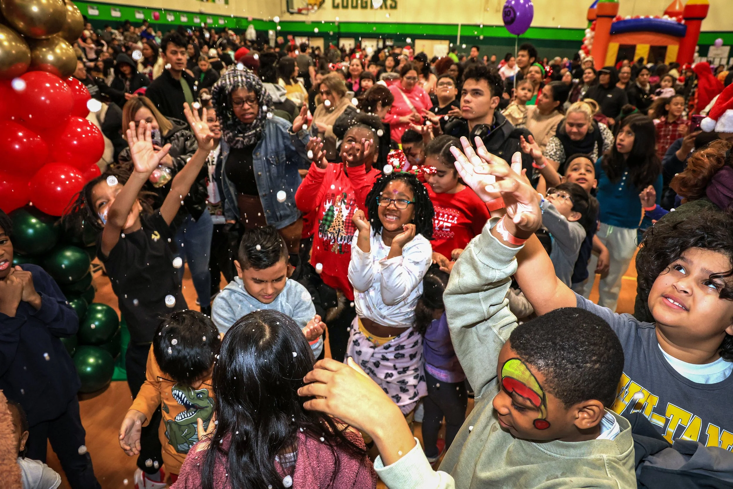 PATERSON, N.J. | 12/24/25: Children play in falling artificial snow bubbles cascading from an upper balcony during the New Jersey Community Development Corporation’s annual Christmas Eve Holiday Party at the Community Charter School of Paterson. The 