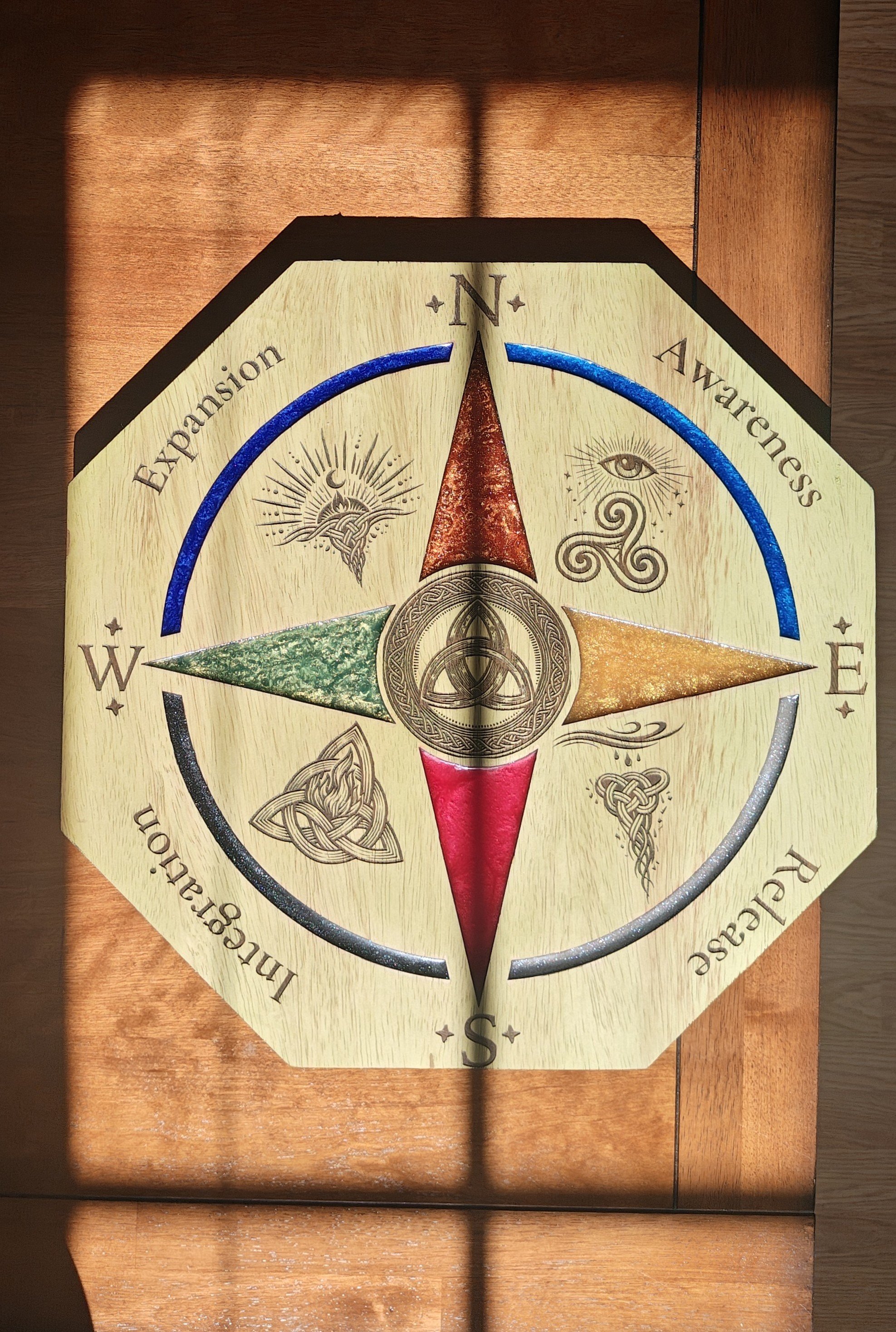 A decorative compass rose with different symbols on a wooden surface, pointing north.