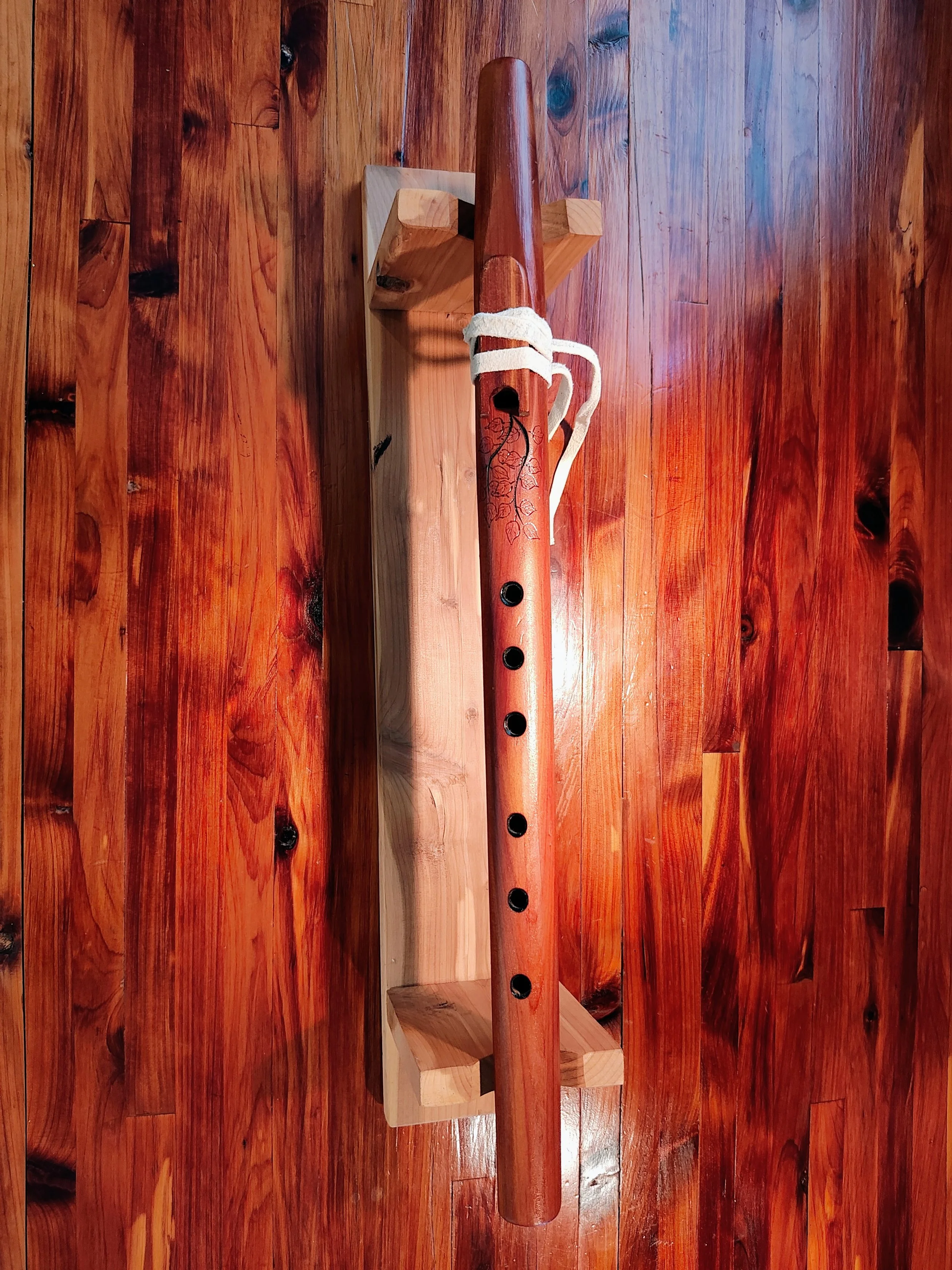 A wooden surface with a table and a decorative native american style wooden flute with leaf and branch patterns resting on a small wooden stand
