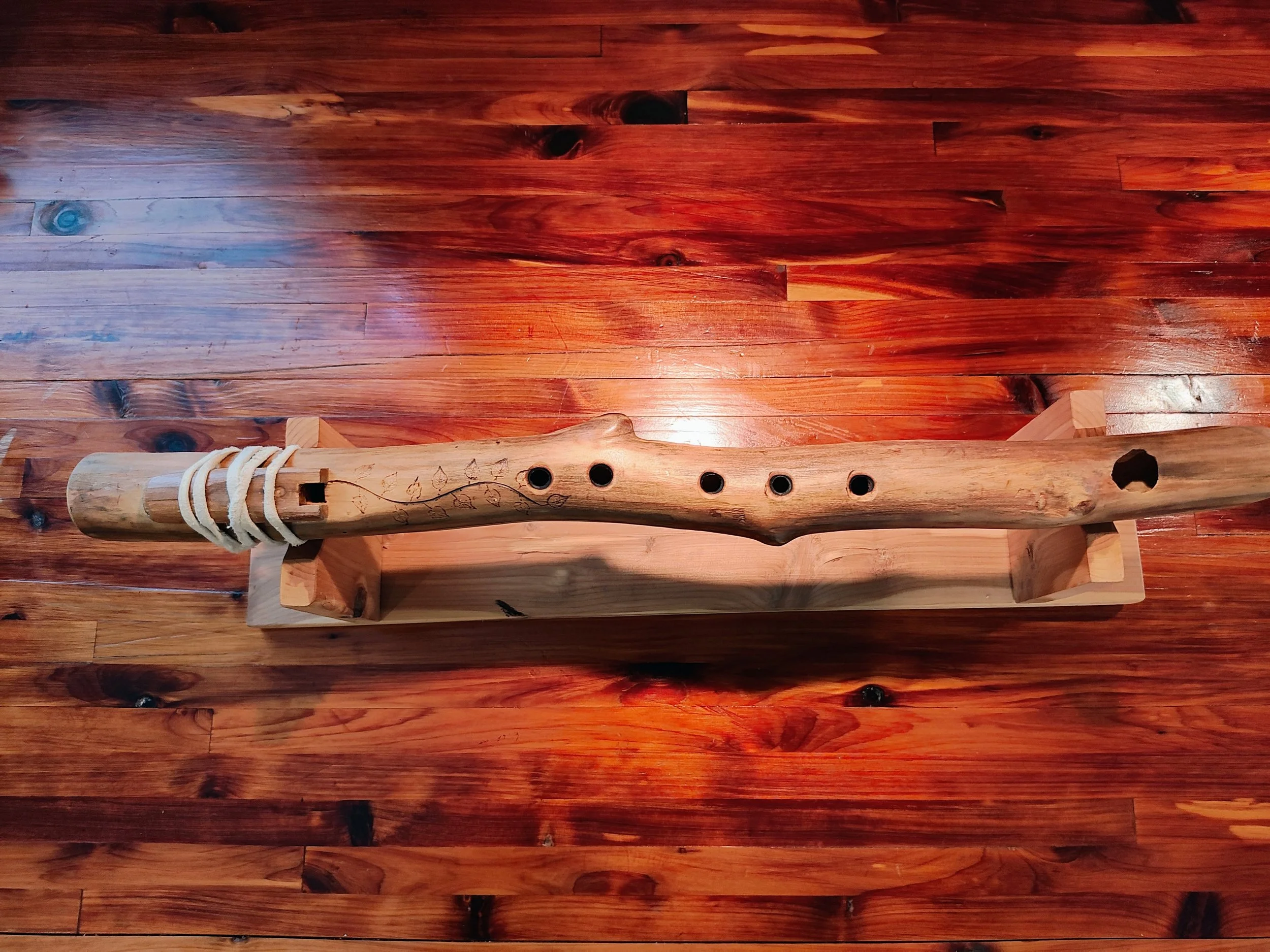 A wooden flute with carved details placed on a wooden floor.