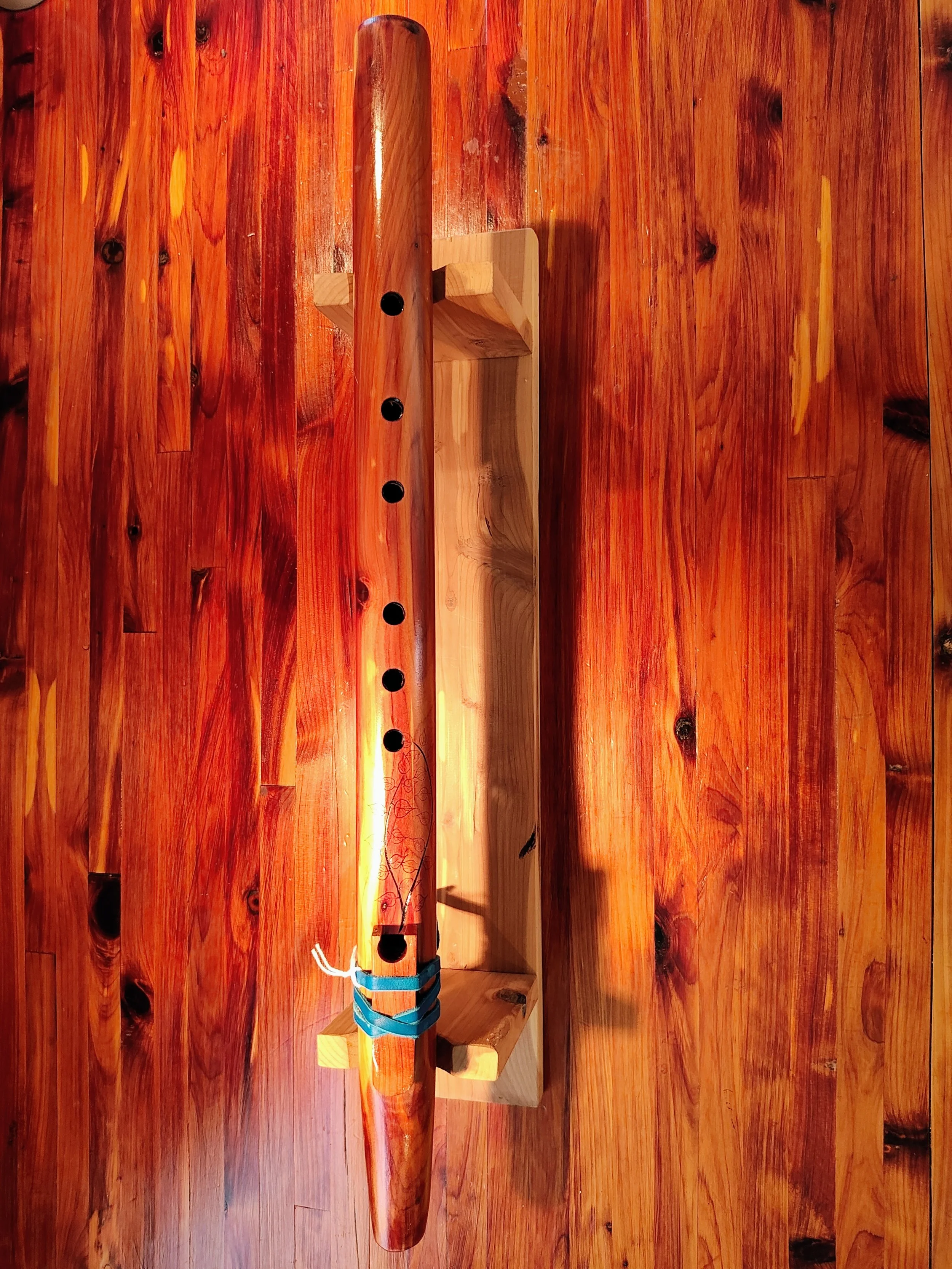A wooden surface with a table and a decorative native american style wooden flute with leaf and branch patterns resting on a small wooden stand