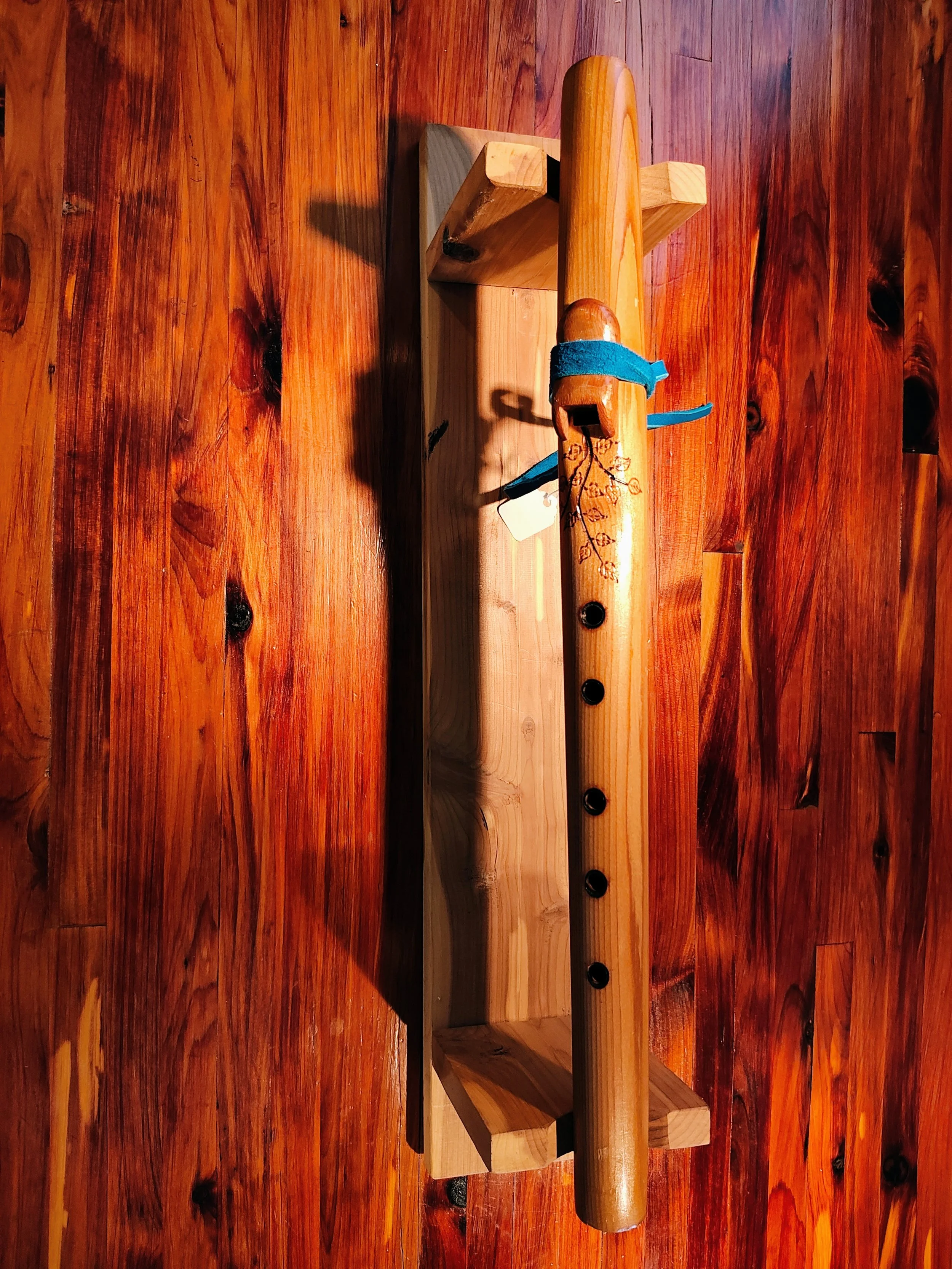 A wooden surface with a table and a decorative native american style wooden flute with leaf and branch patterns resting on a small wooden stand