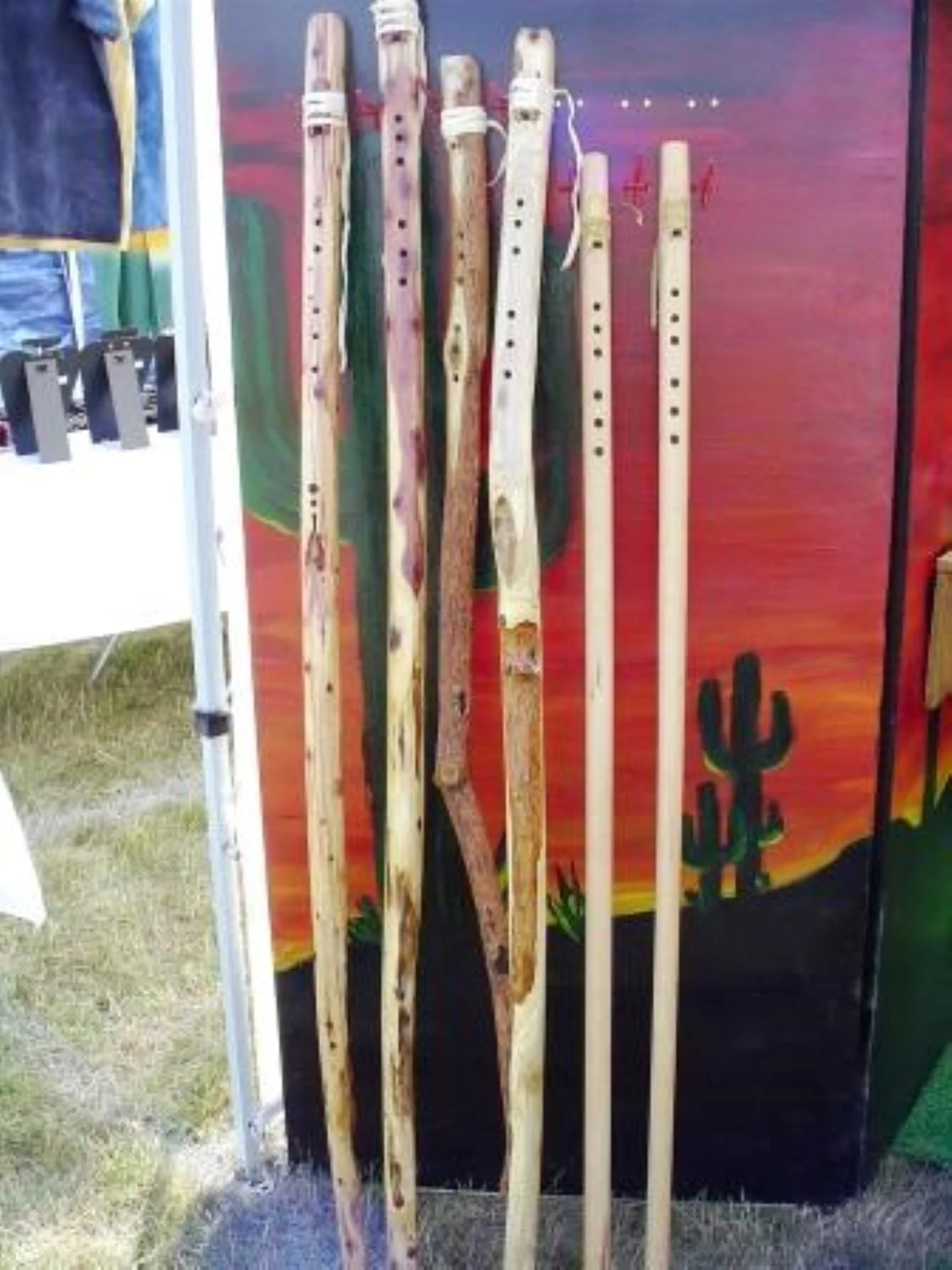 A display of wooden flutes standing vertically in front of a colorful desert landscape background with cacti and mountains.