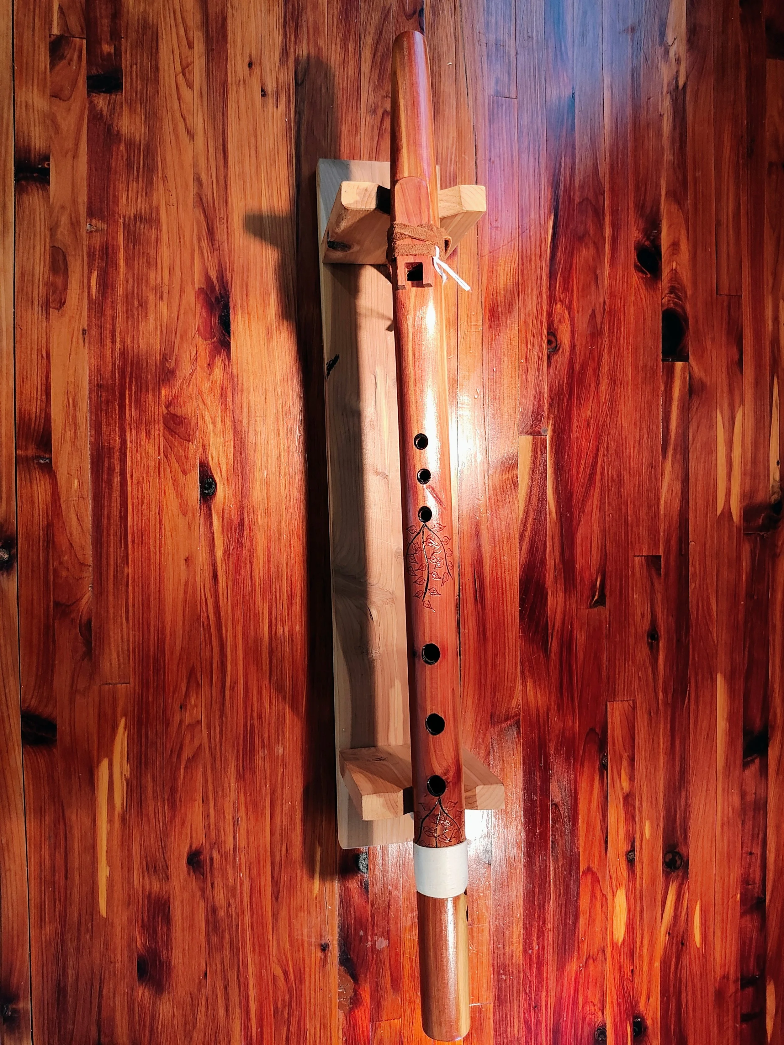 A wooden surface with a table and a decorative native american style wooden flute with leaf and branch patterns resting on a small wooden stand