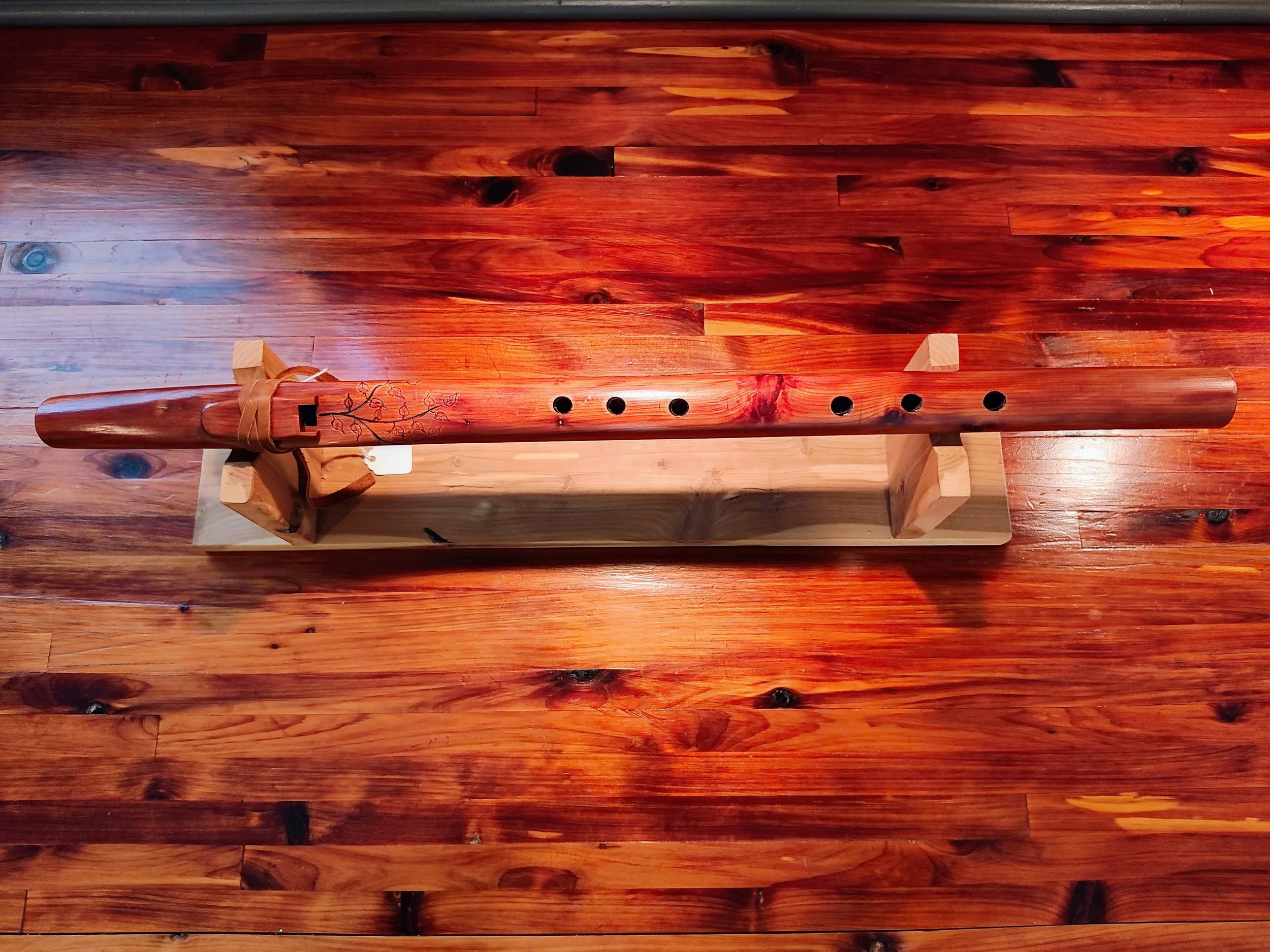 A wooden floor with a long, decorative wooden musical instrument resting on a wooden stand.