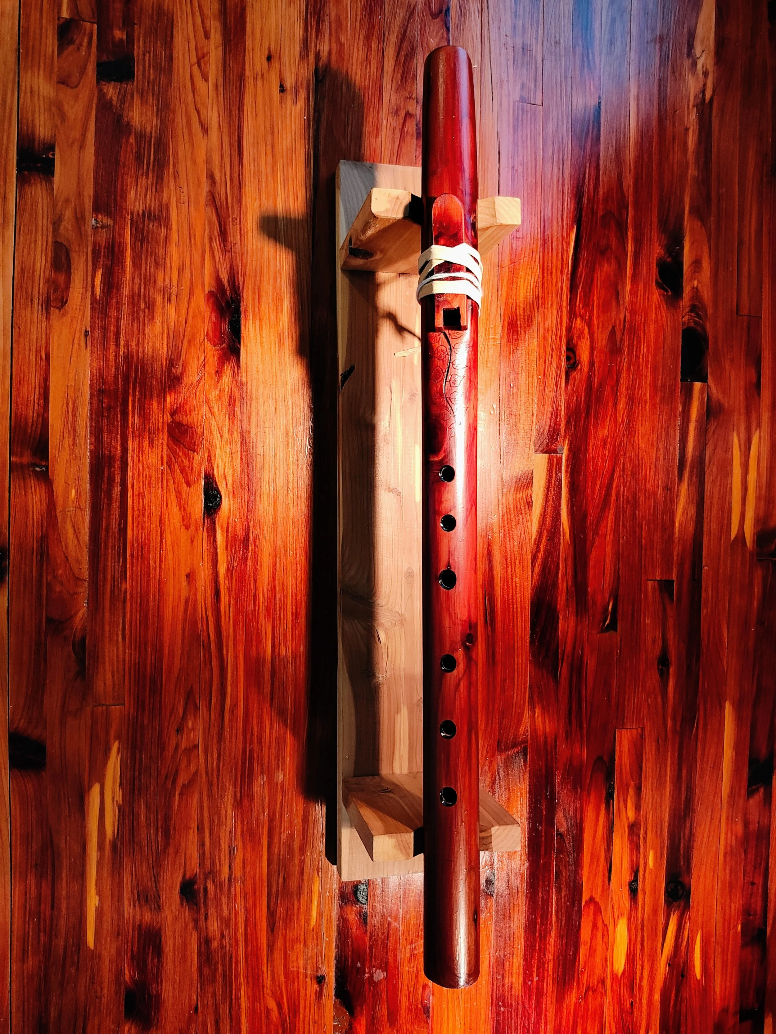 A wooden surface with a table and a decorative native american style wooden flute with leaf and branch patterns resting on a small wooden stand