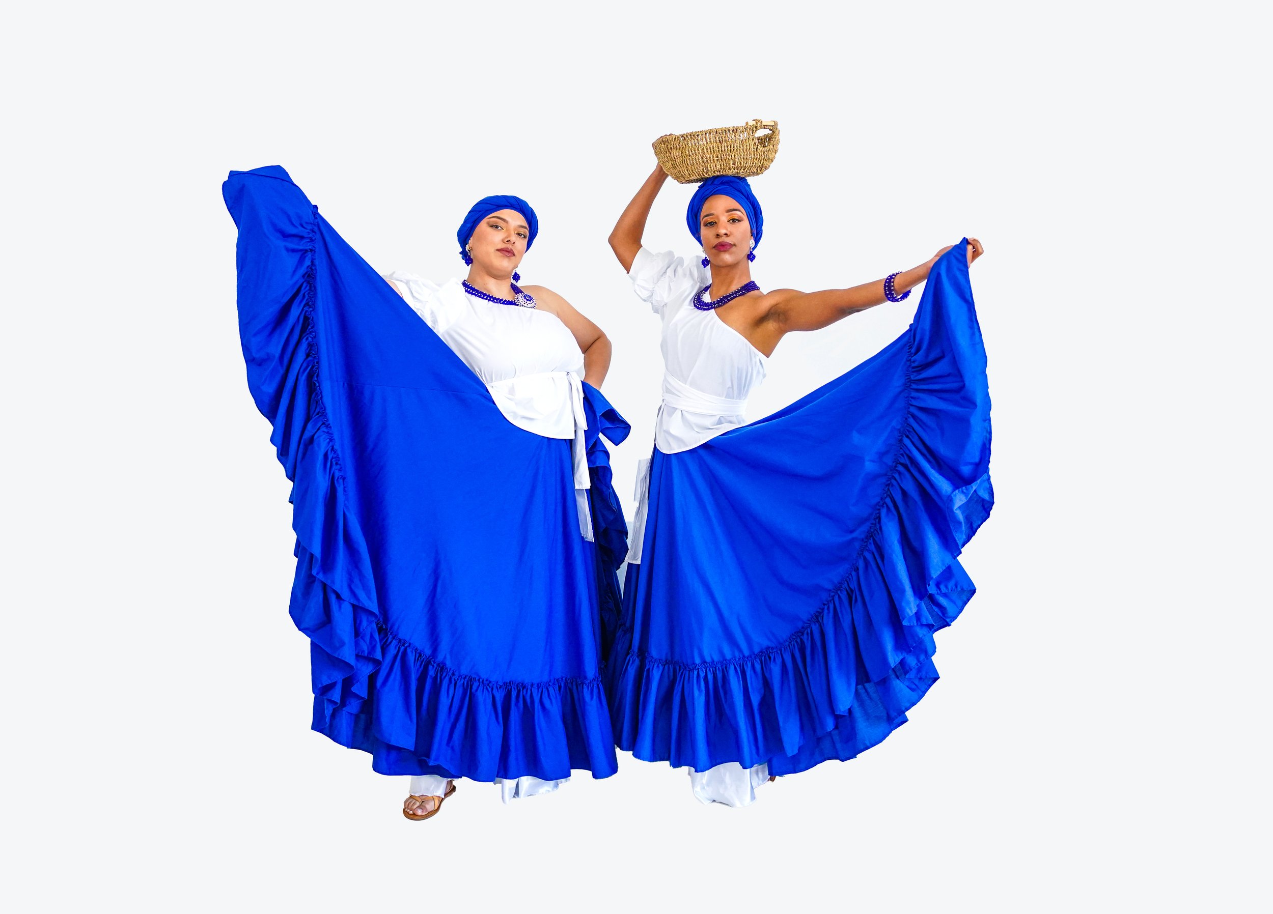 Two women wearing white blouses, blue skirts, and blue headwraps, holding their skirts out to the sides, one woman balances a basket on her head, against a plain white background.