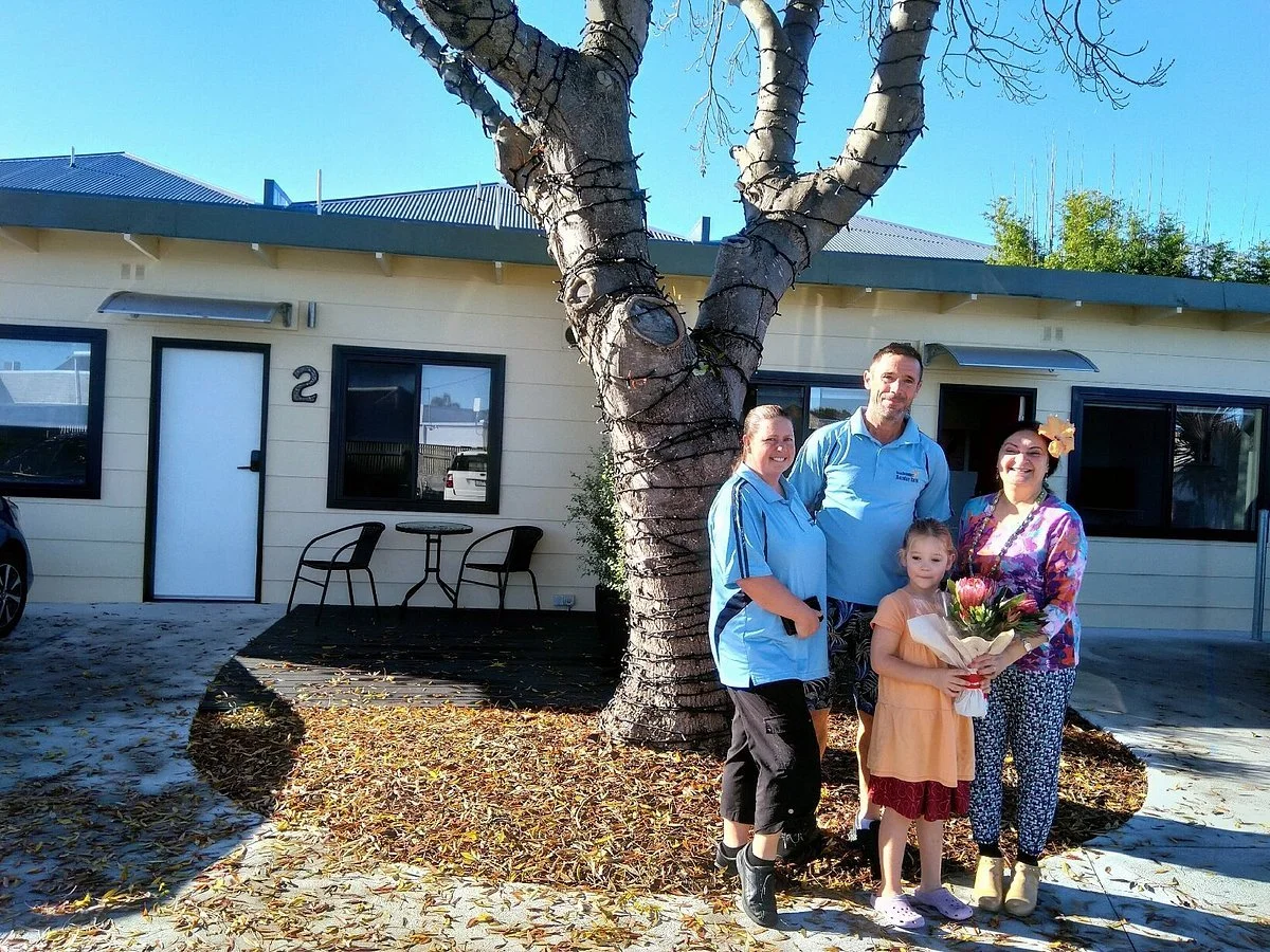 Rebecca, Marty and Matilda in photo handing flowers to guest in front of units