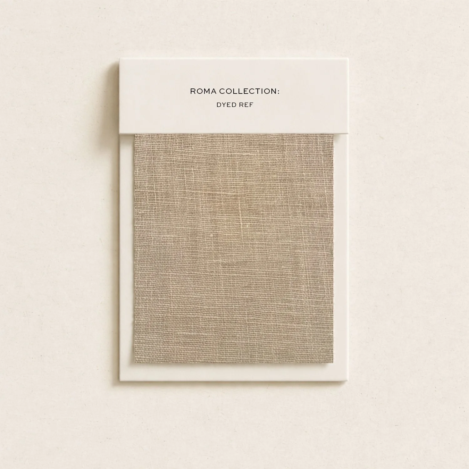Fabric sample card labeled 'Roma Collection; Dyed Ref' with beige fabric swatch in white frame, hanging on a wall.