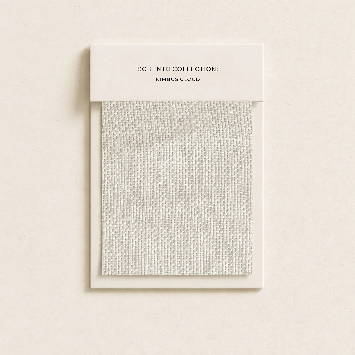 A sample swatch of fabric with a small rectangular paper label on top that reads "Sorento Collection: Nimbus Cloud".