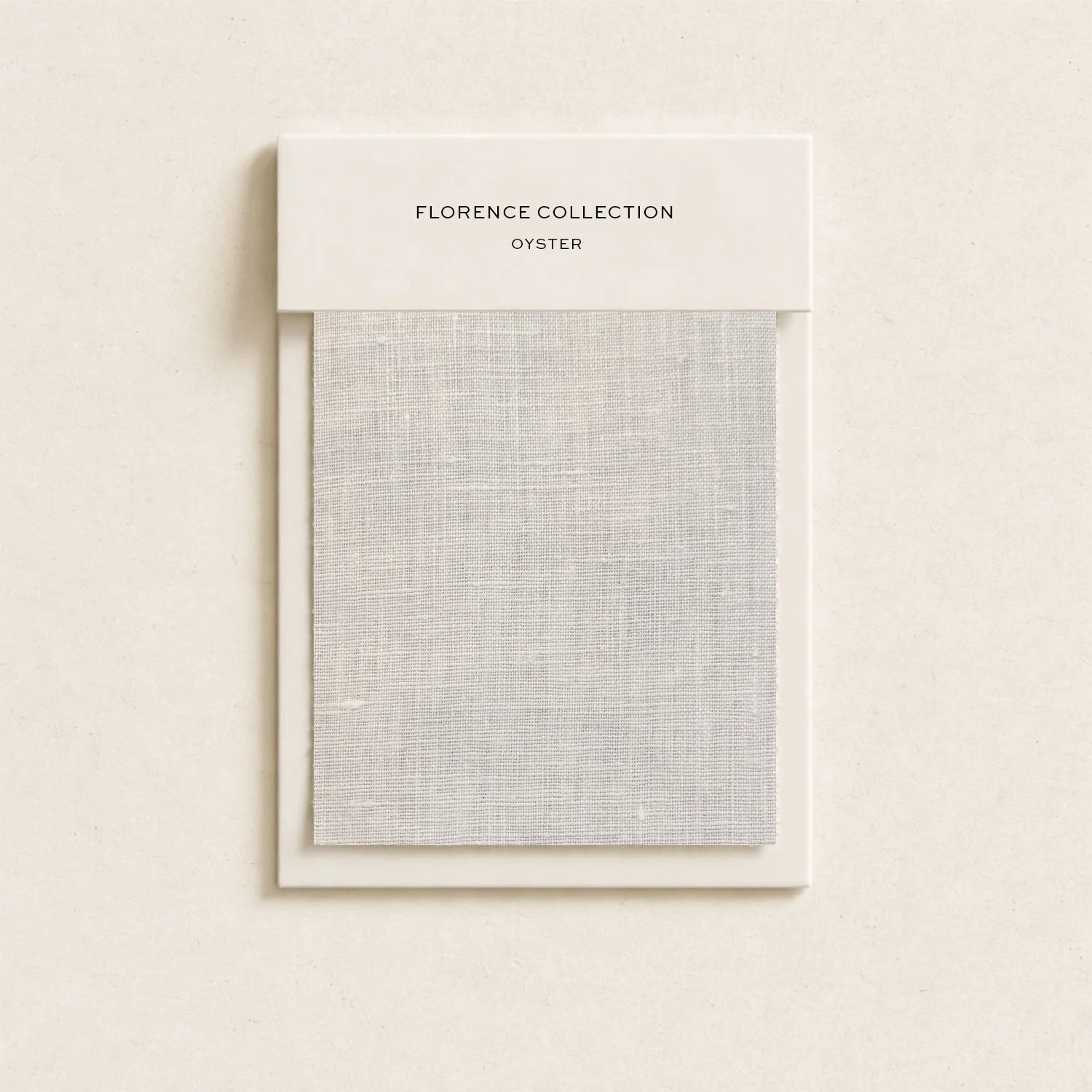 A fabric swatch sample labeled 'Florence Collection Oyster' in a white frame, hanging on a beige wall.