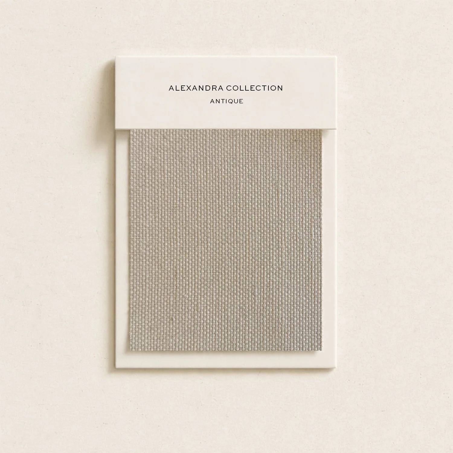 A beige fabric swatch sample with a white border, mounted on a white card that reads 'Alexandra Collection Antique'.