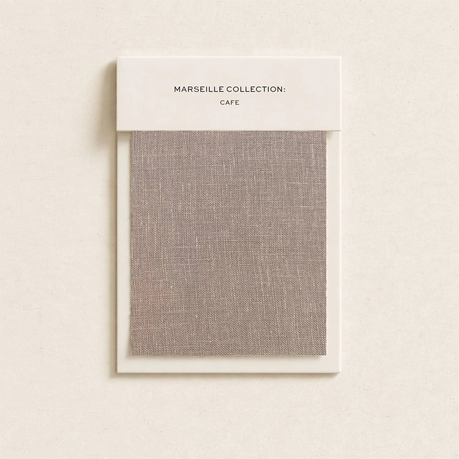 Close-up of a framed fabric swatch sample with a label reading "Marseille Collection: Cafe" on a plain white background.