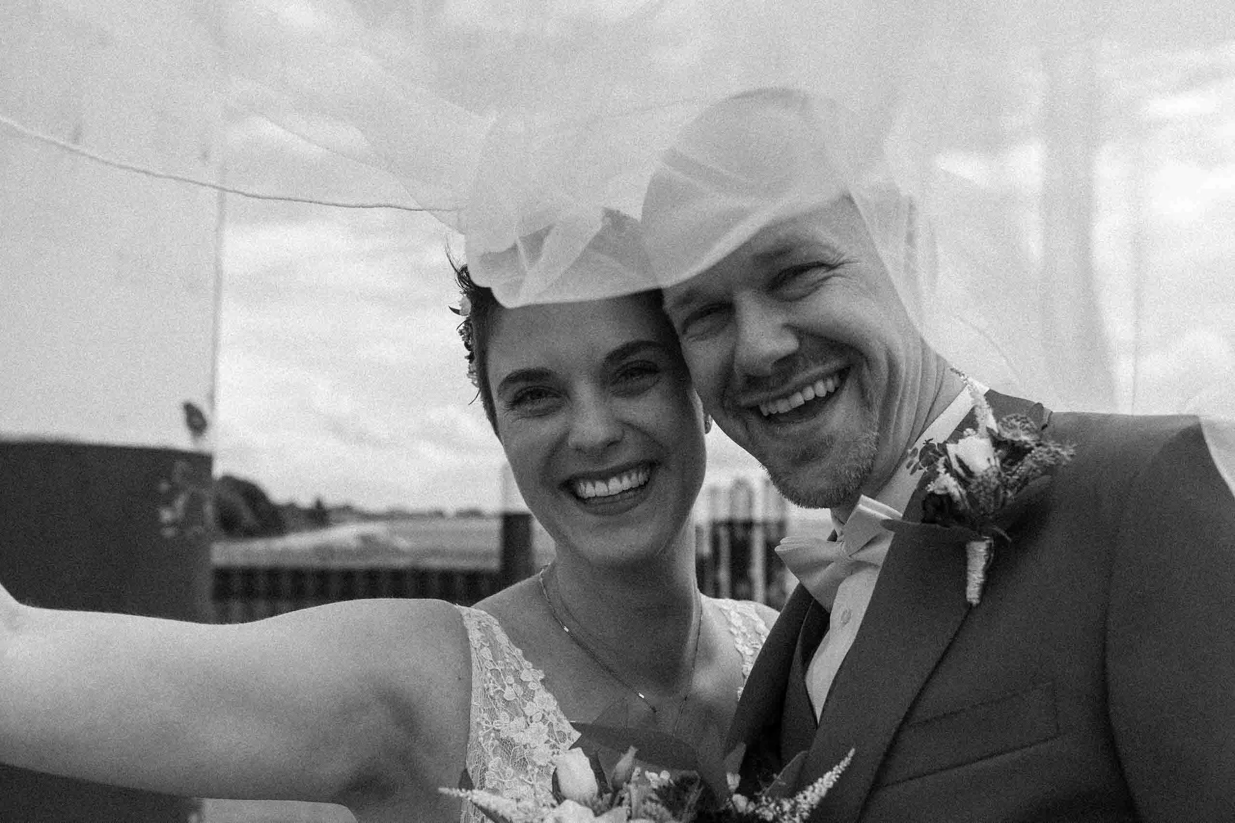 Ein glückliches Paar, das bei ihrer Hochzeit Fotos macht, in formeller Kleidung, lächelnd, an einem Tag mit bewölktem Himmel.