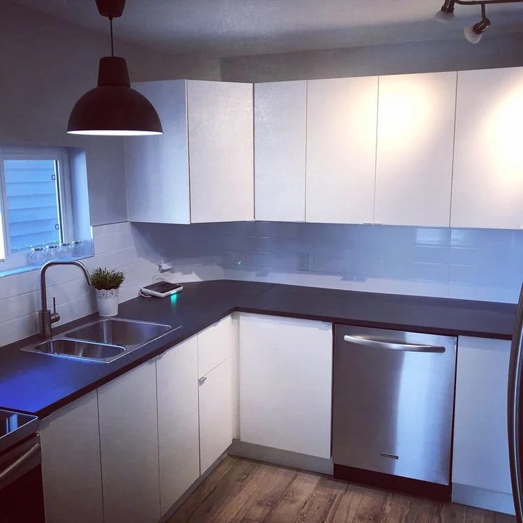 Modern kitchen with white cabinets, black countertop, stainless steel sink, small window, potted plant, and stainless steel dishwasher. kitchen contractor, cabinet installer, appliance installer, drywall contractor, contractor.
