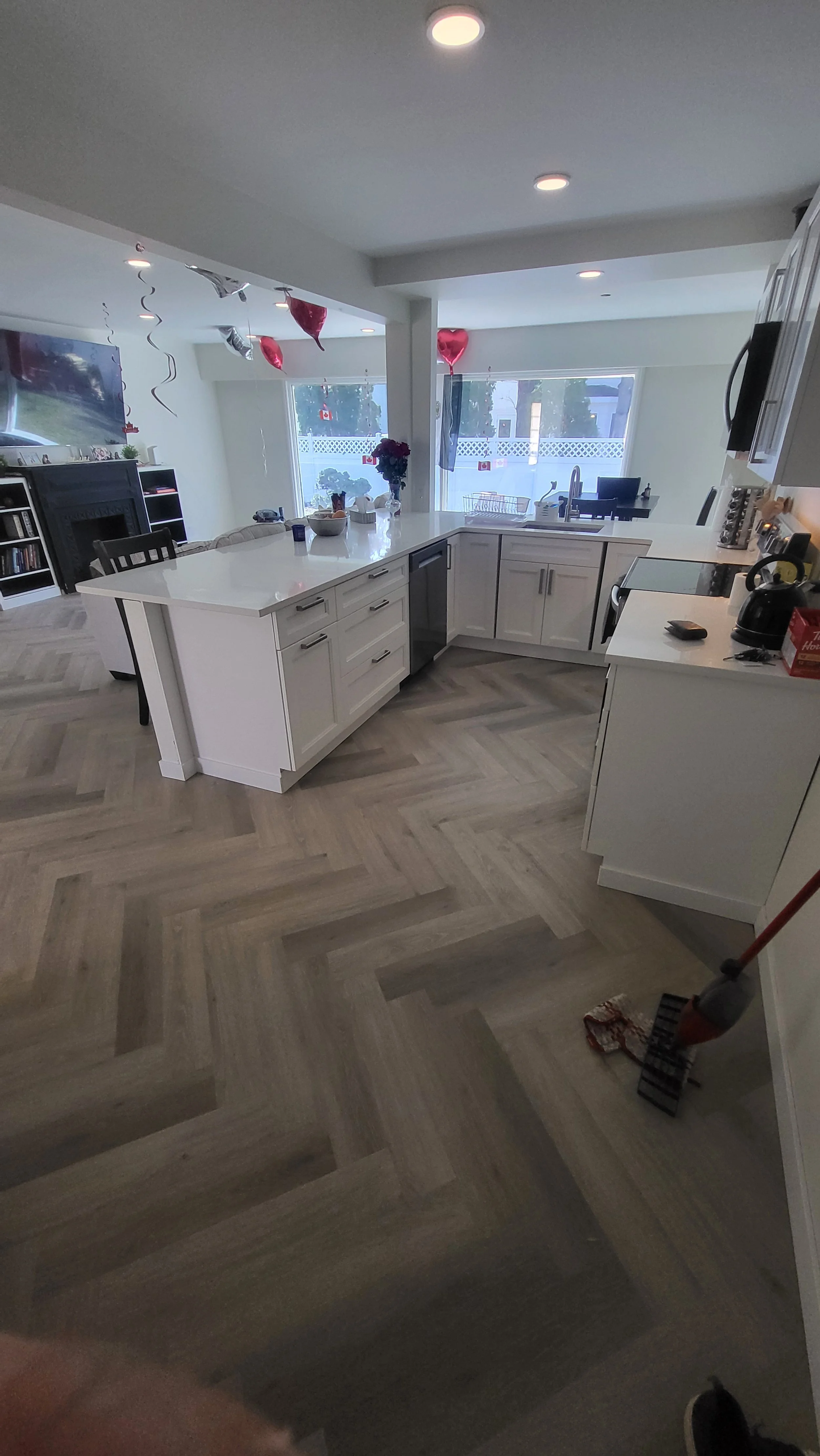 Interior of a modern kitchen with white cabinets, a large island, and a view of the living room decorated with balloons for a celebration. Kitchen remodel, flooring installer.