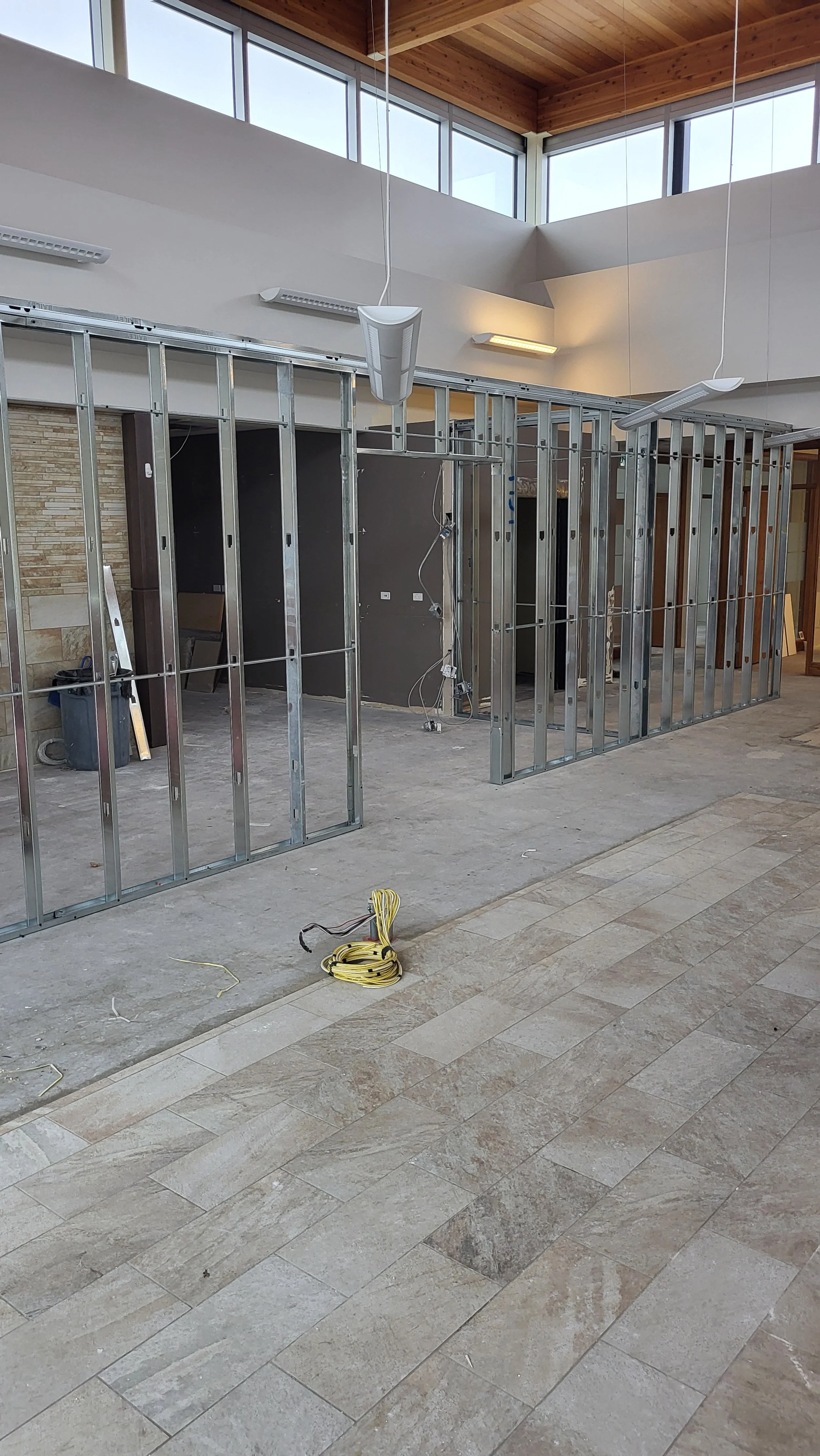 Interior of a building under construction with metal framing for walls, electrical wiring, and large windows near the ceiling.