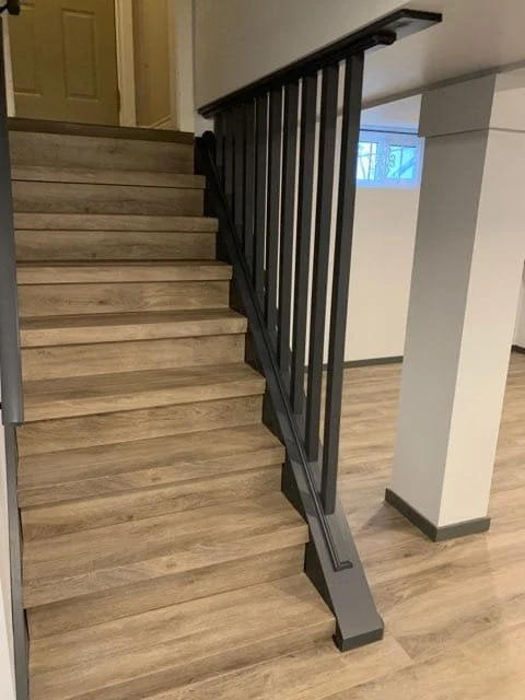 Interior staircase with wooden steps and a black metal railing.  Basement Renovation, hardwood floors, construction, drywall contractor, painter, framer, stair installer