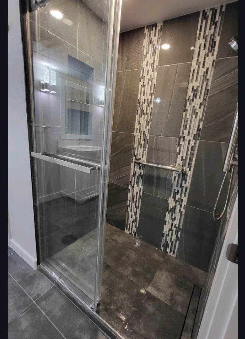 Modern shower with dark gray stone tiles, decorative vertical tile strips, and glass door. Bathroom Contractor, tile contractor, contractor, glass door installer, renovation