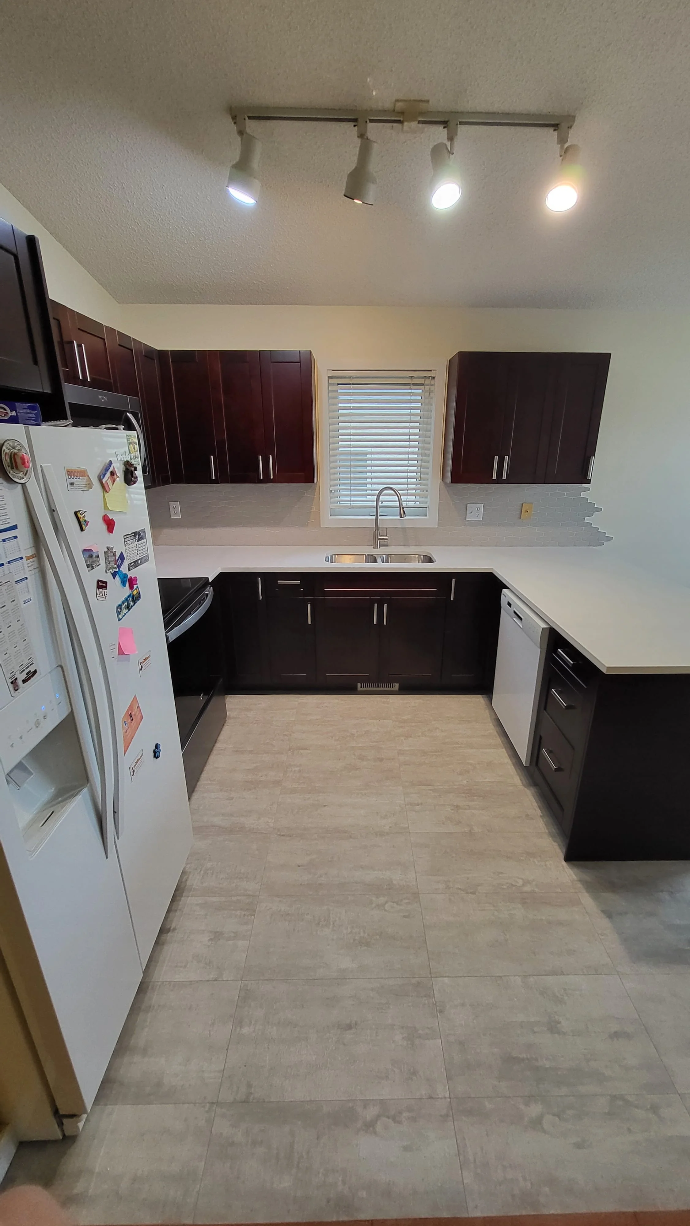 Kitchen with dark wood cabinets, white countertops, a window above the sink, and appliances including a refrigerator, dishwasher, and stove. kitchen contractor, cabinet installer, appliance installer, drywall contractor, contractor.