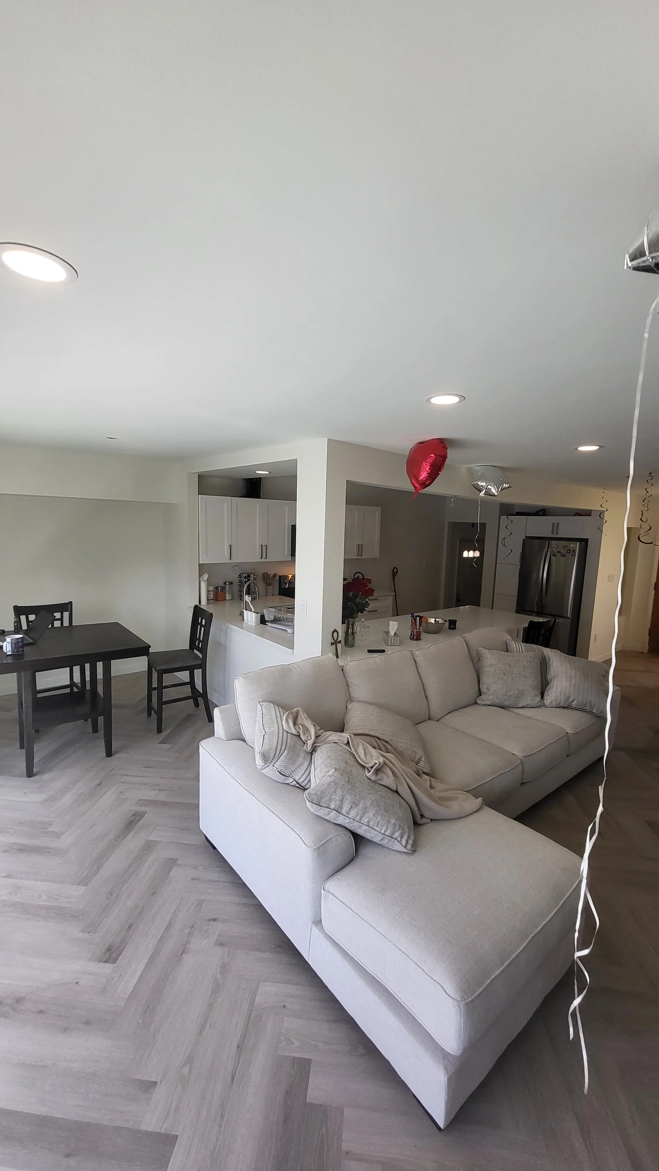 Living room with a beige sectional sofa, balloons hanging from the ceiling, and a dining table with black chairs in the background. kitchen contractor, cabinet installer, appliance installer, drywall contractor, contractor.