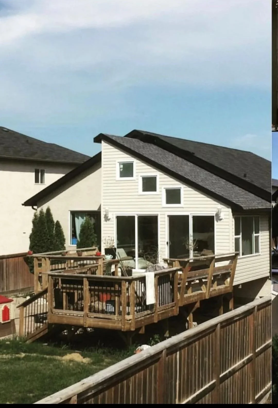 A white house with a wooden deck and a fenced backyard. Home addition construction.