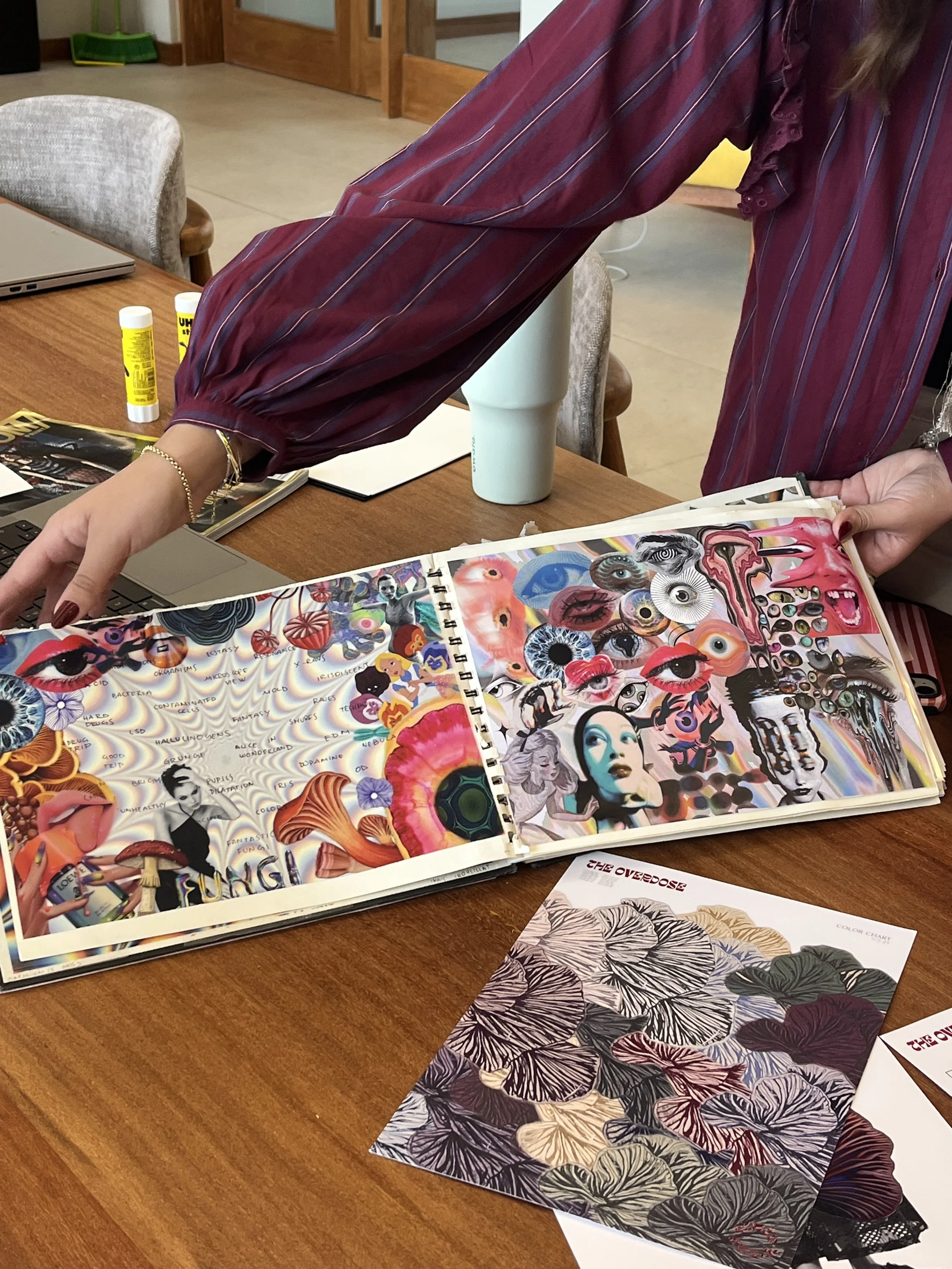 Libro con páginas llenas de arte psicodélico y collage de ojos, rostros y patrones coloridos en una mesa de madera, con dos botes de pegamento y papeles decorativos a la vista.