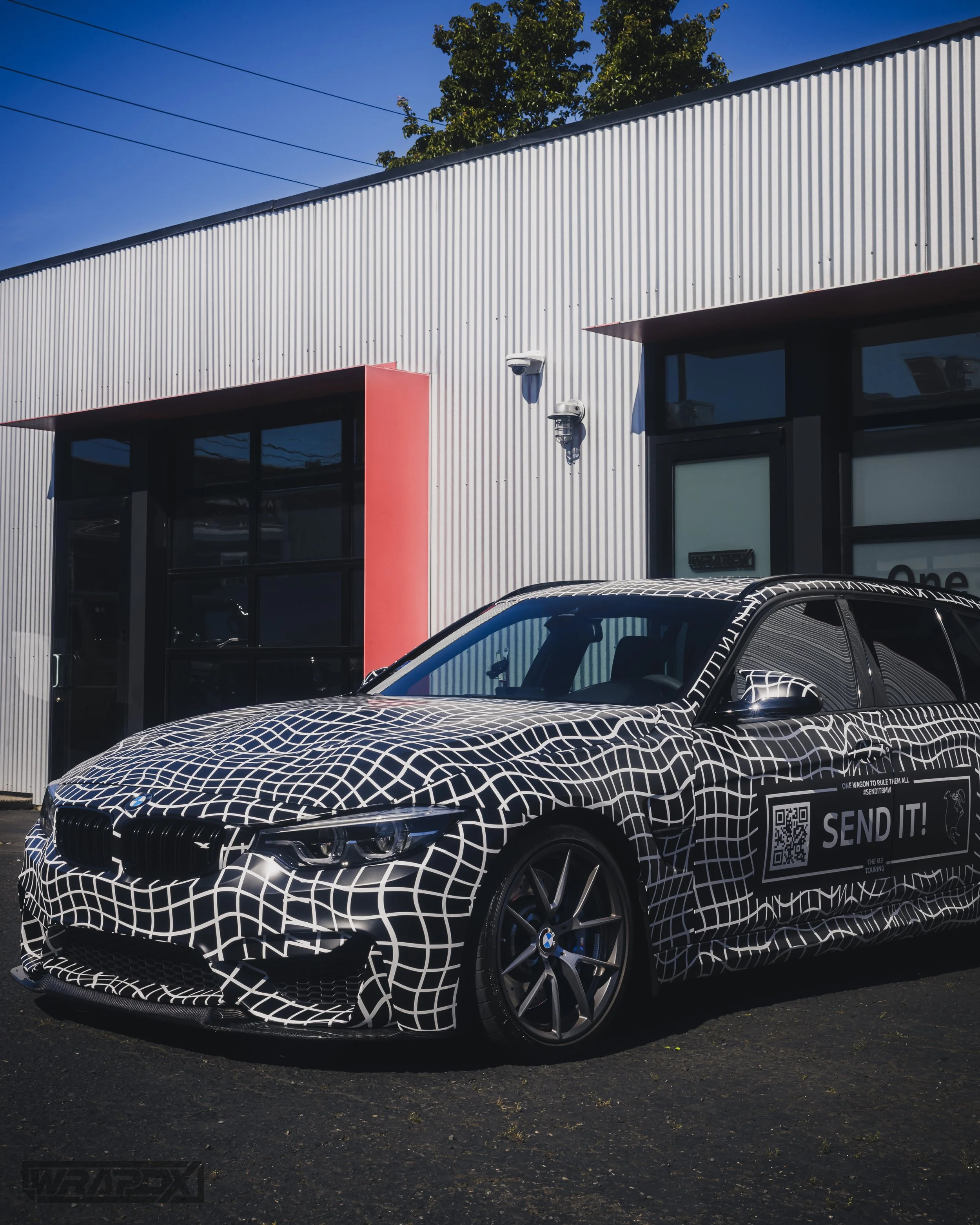 Car wrapped in geometric pattern parked outside a building.