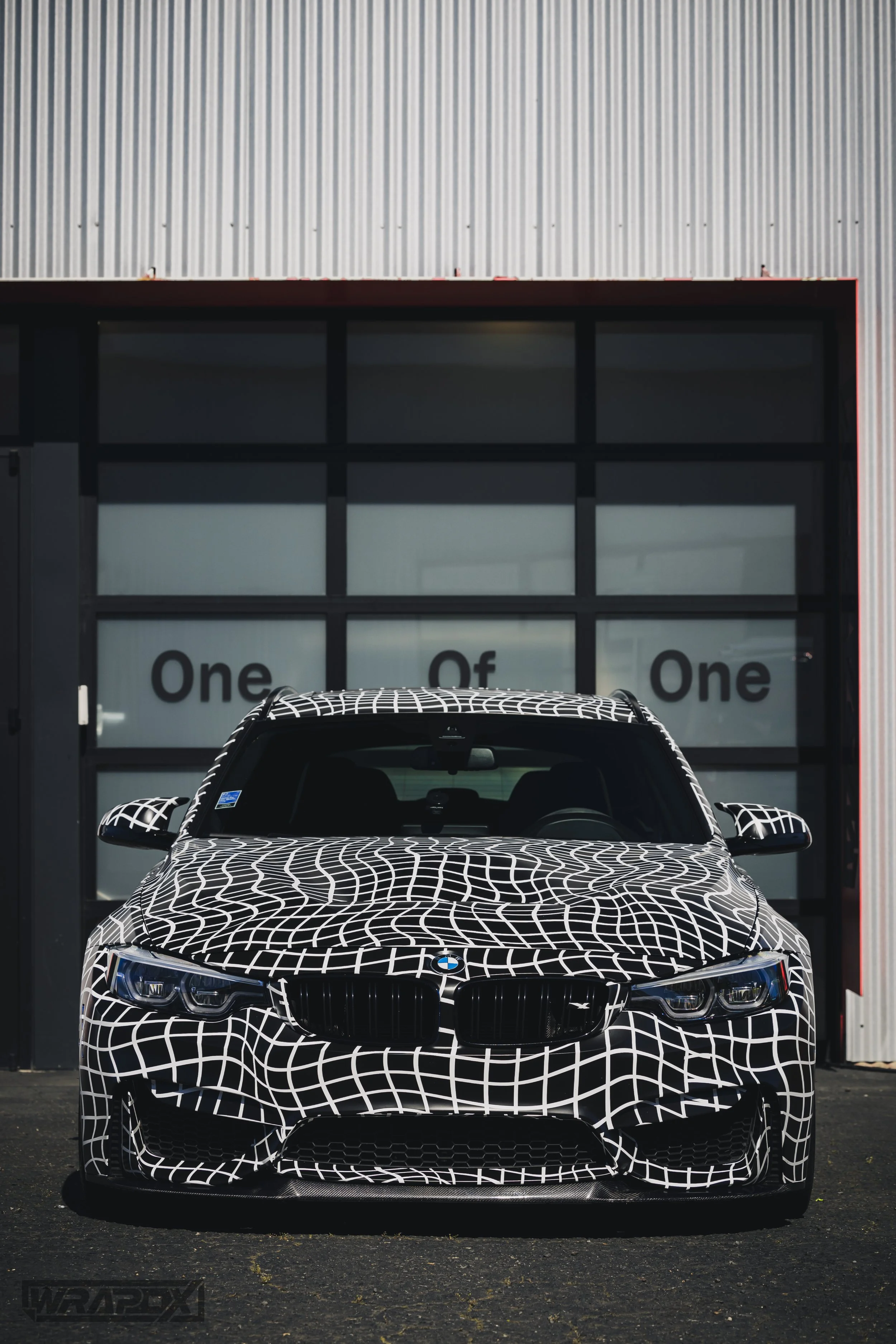 BMW car with black and white geometric wrap in front of industrial building.