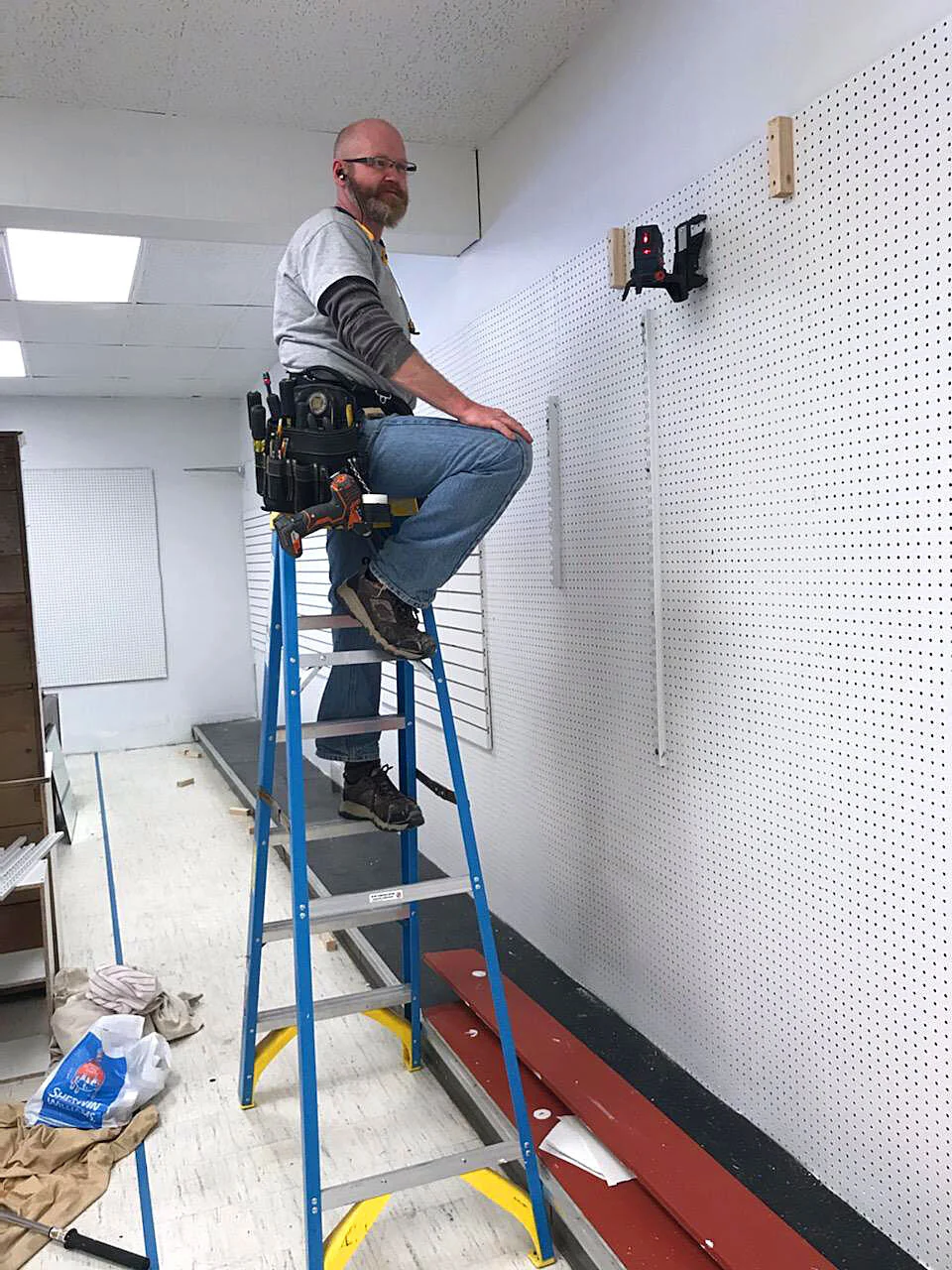 A volunteer works on the finishing touches of a pegboard wall.