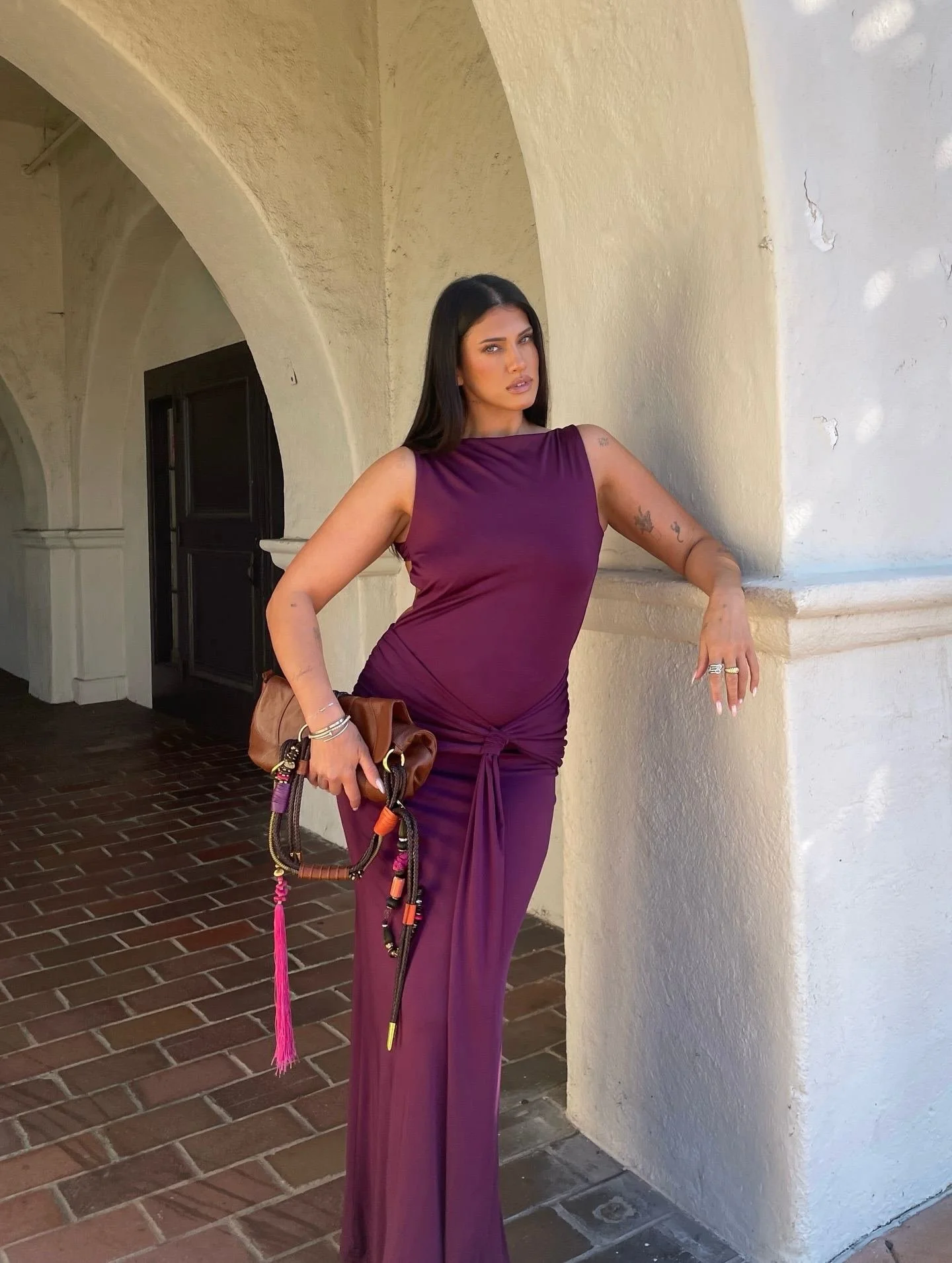 Woman in a purple dress posing near a white stucco wall with arches.
