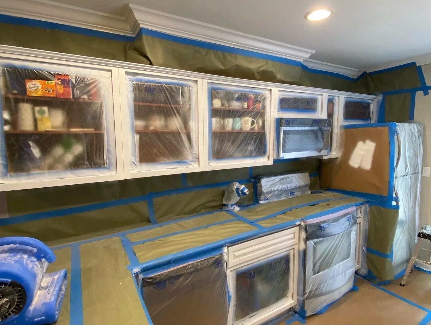 Kitchen cabinets and appliances covered with plastic and painter's tape for painting renovations.