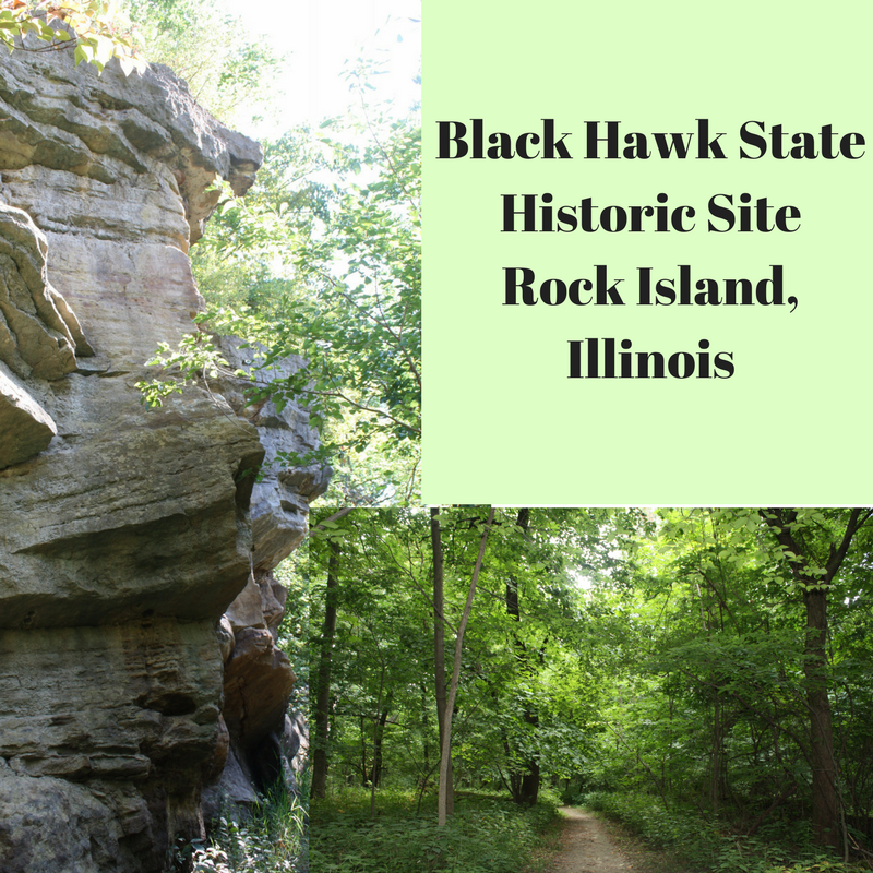 Sign indicating Black Hawk State Historic Site, Rock Island, Illinois, with a forested trail and rock formation in the background.