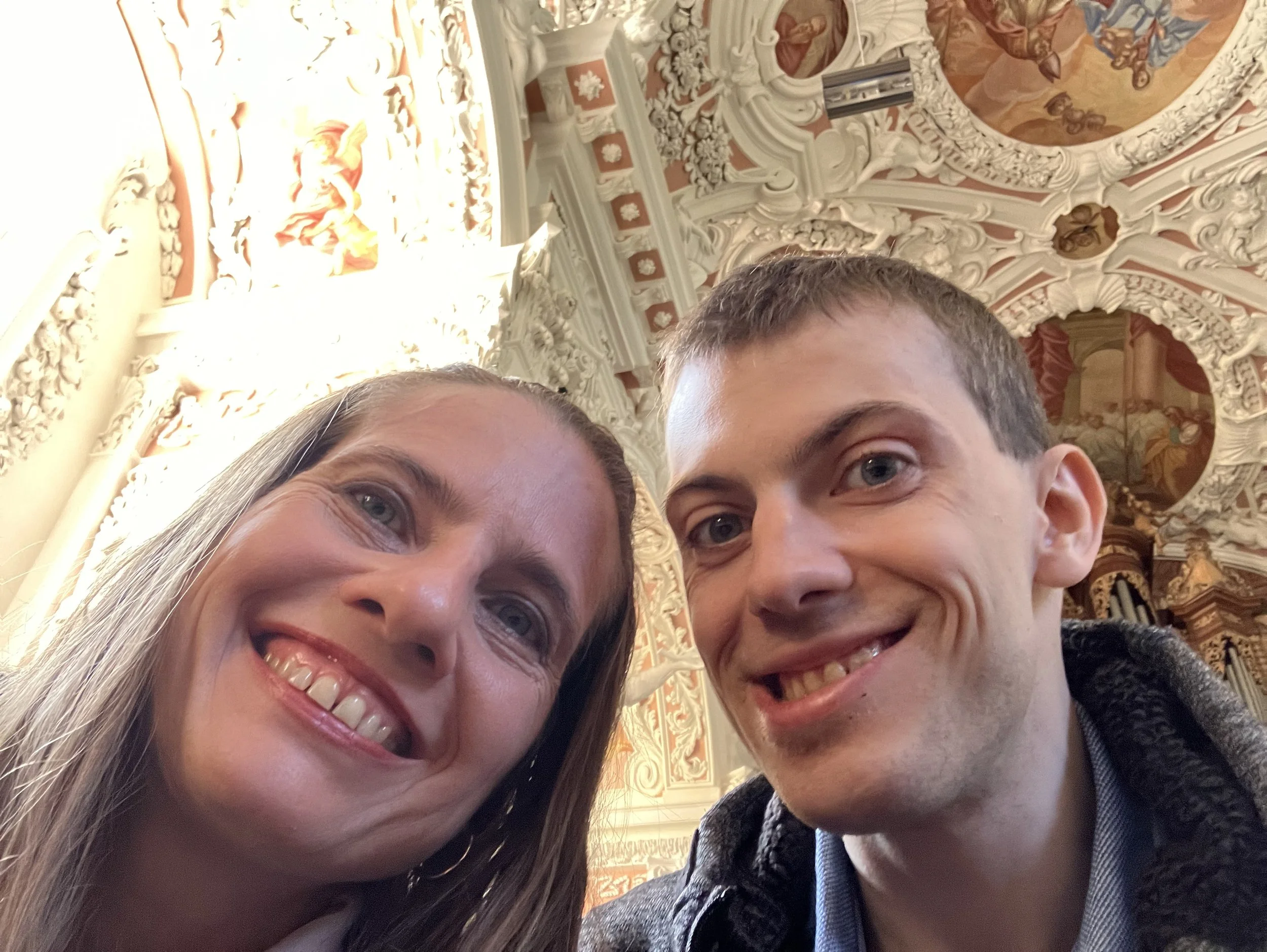 Katrina and her son taking a selfie inside a richly decorated, ornate building with elaborate stucco work and ceiling paintings.