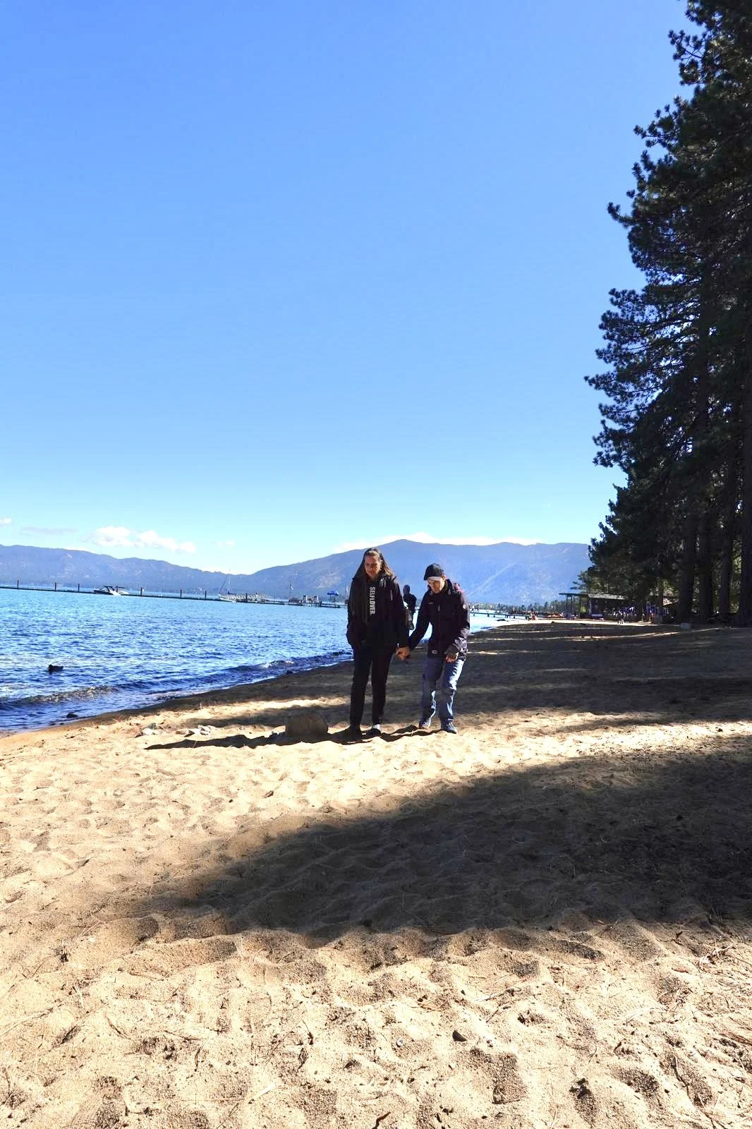 Katrina and her son are walking along a sandy beach holding hands with mountains and a body of water in the background.