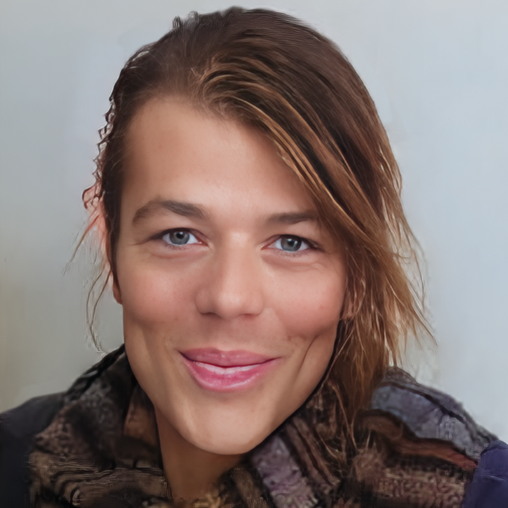 Close-up portrait of Secondary Media LLC Sole Proprietor with light skin, shoulder-length brown hair with a side part, blue eyes, and a bright smile, wearing a dark patterned scarf against a plain light background.