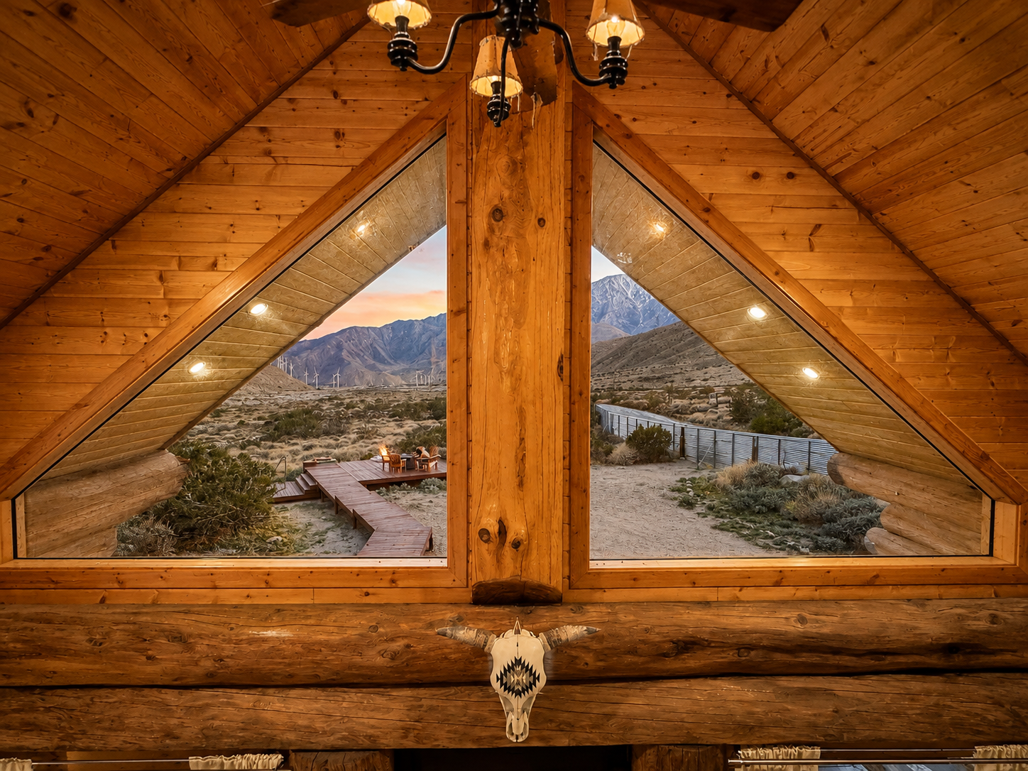 A-frame gable window framing the desert deck and mountains at sunset