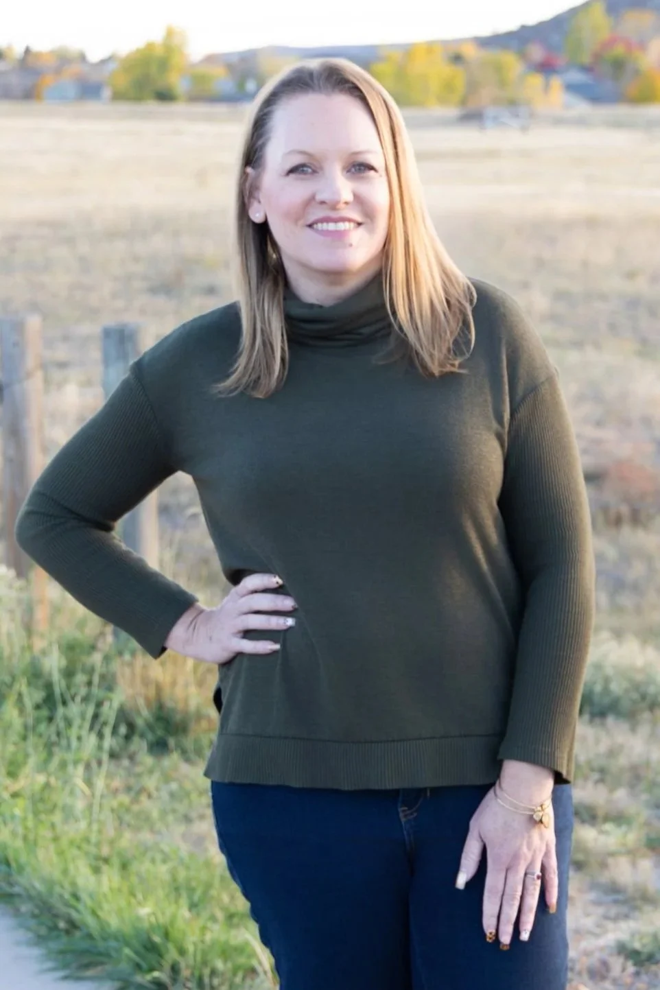 Close-up of colorful daisies in pink, white, yellow, and purple with green leaves, laid on a wooden surface.