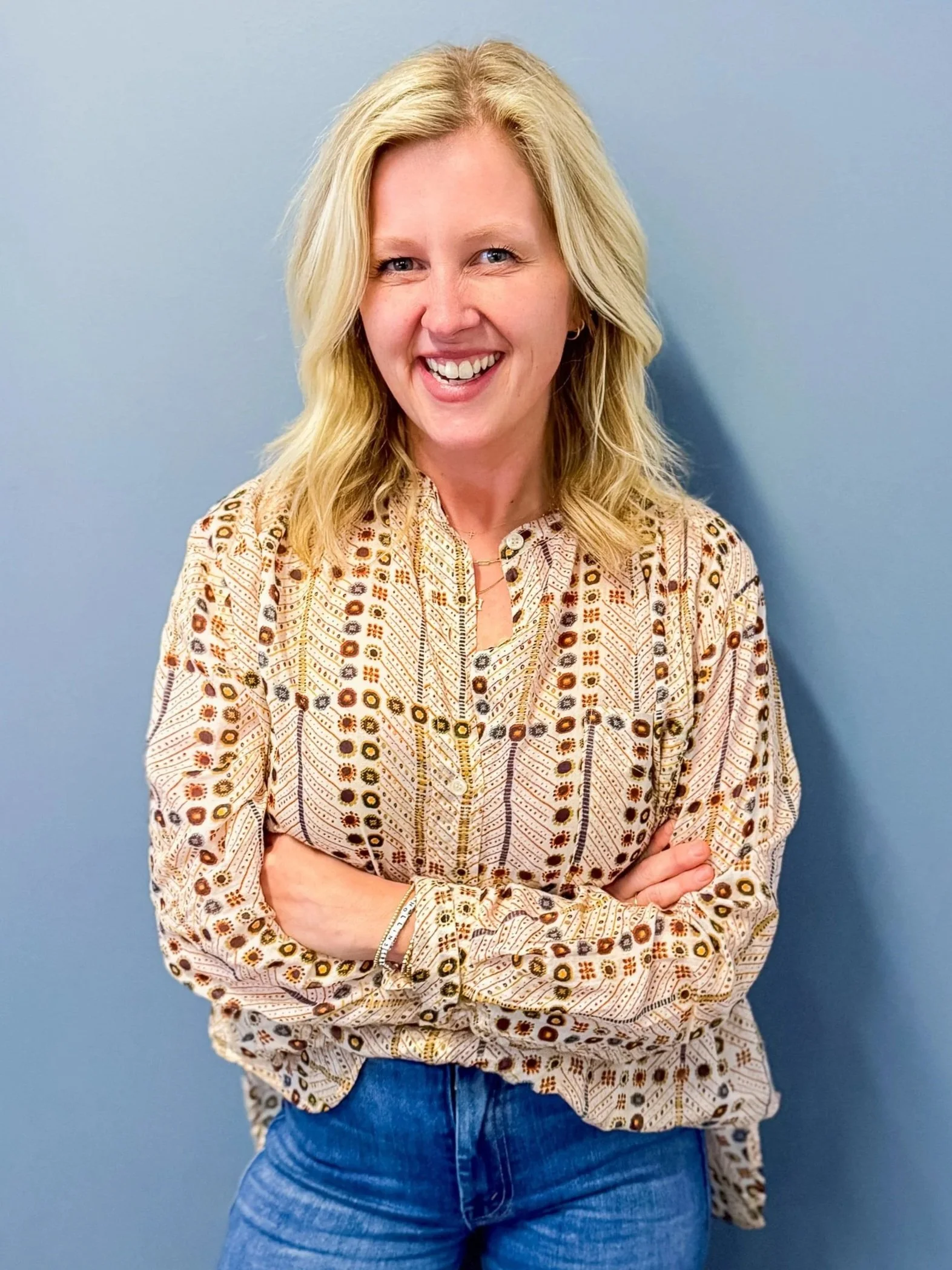Portrait of a woman with long blonde hair smiling while standing against a blue wall