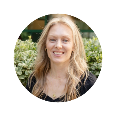 A woman with long blonde hair smiling outdoors, wearing gold hoop earrings and a black top, with greenery in the background who provides OCD treatment and therapy in San Diego, CA. 