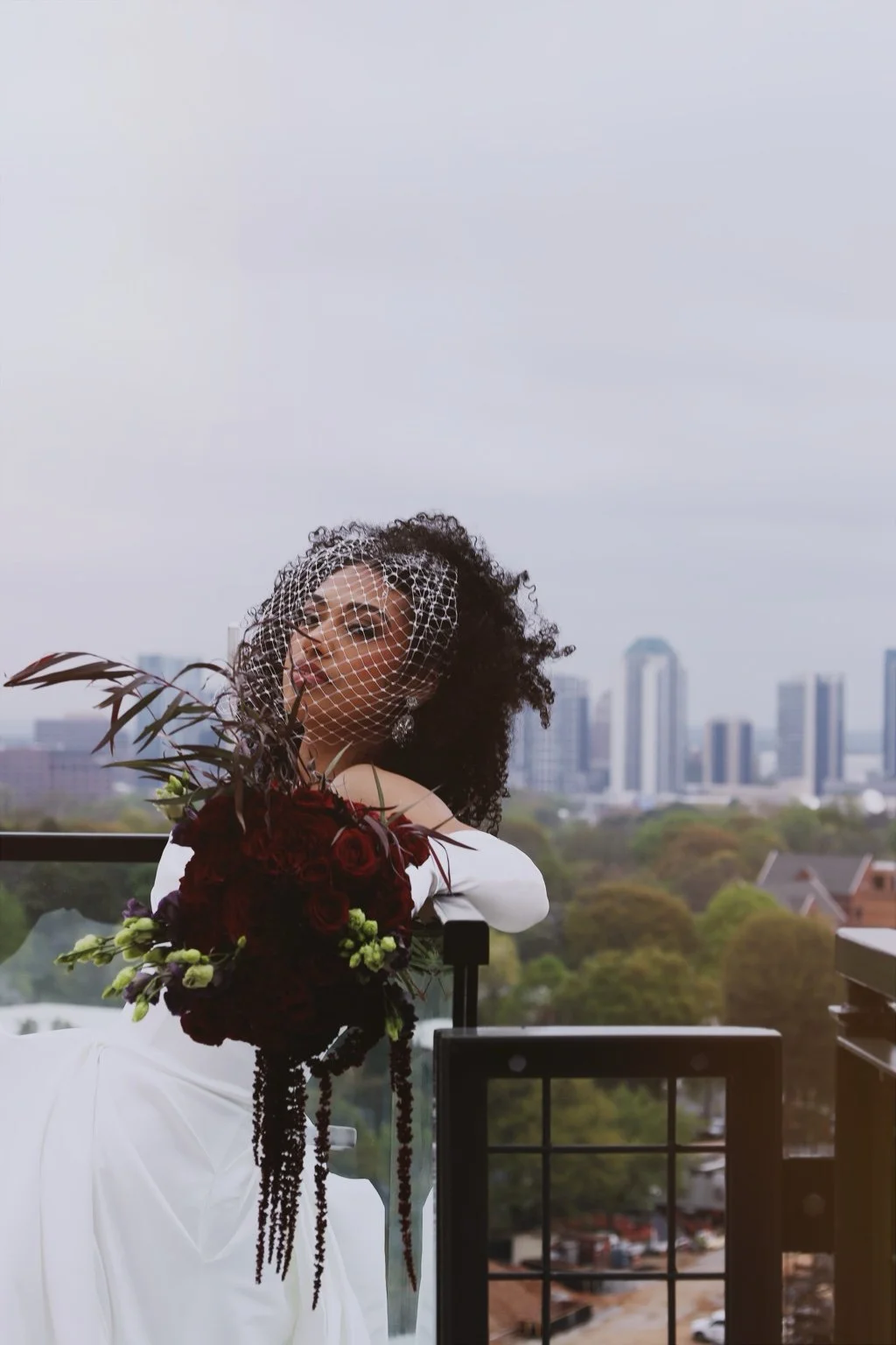Bride in a wedding gown holding a bouquet on a rooftop overlooking the city.