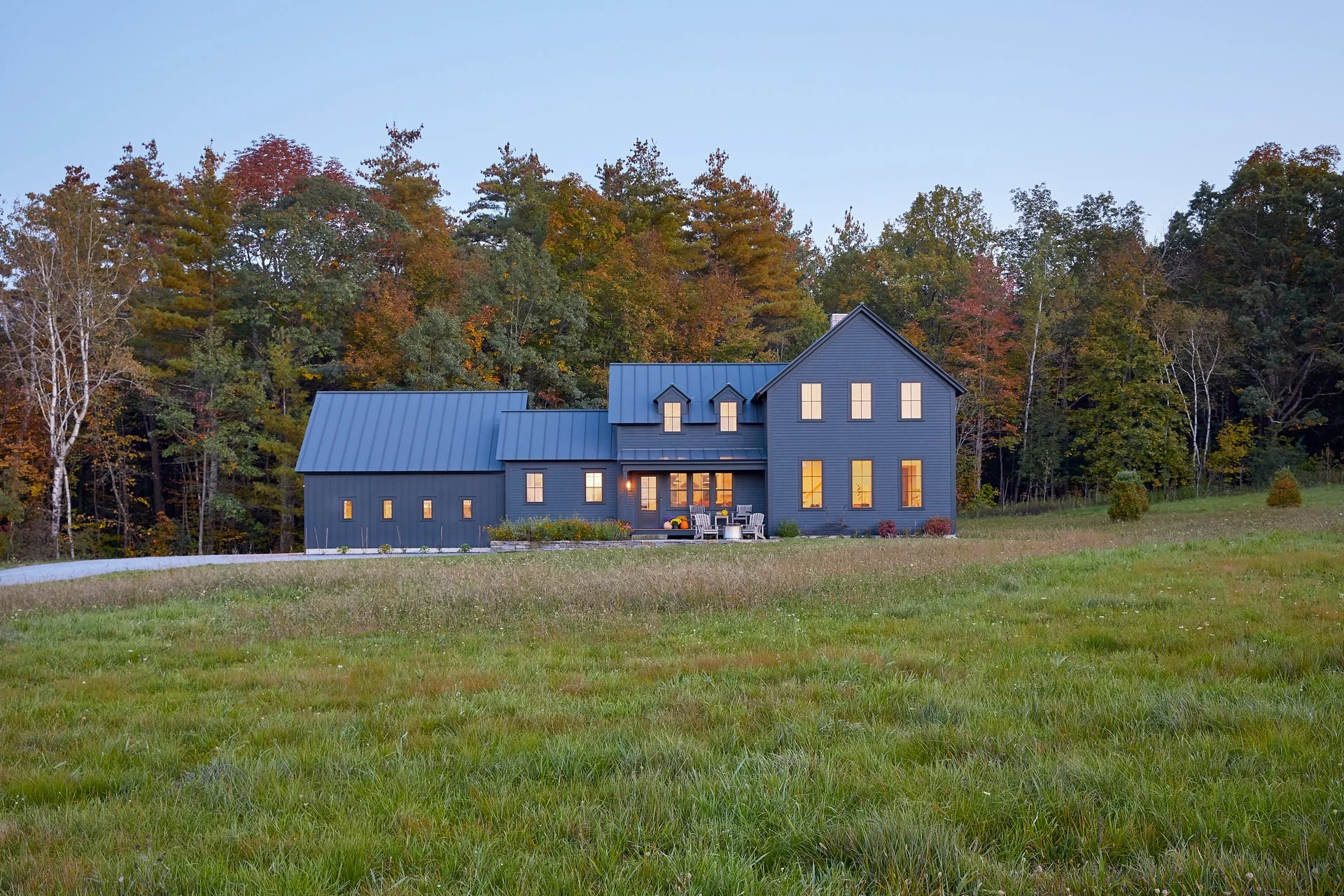 Landscape view of a black toned home with long yellow windows featuring the green surrounding area.