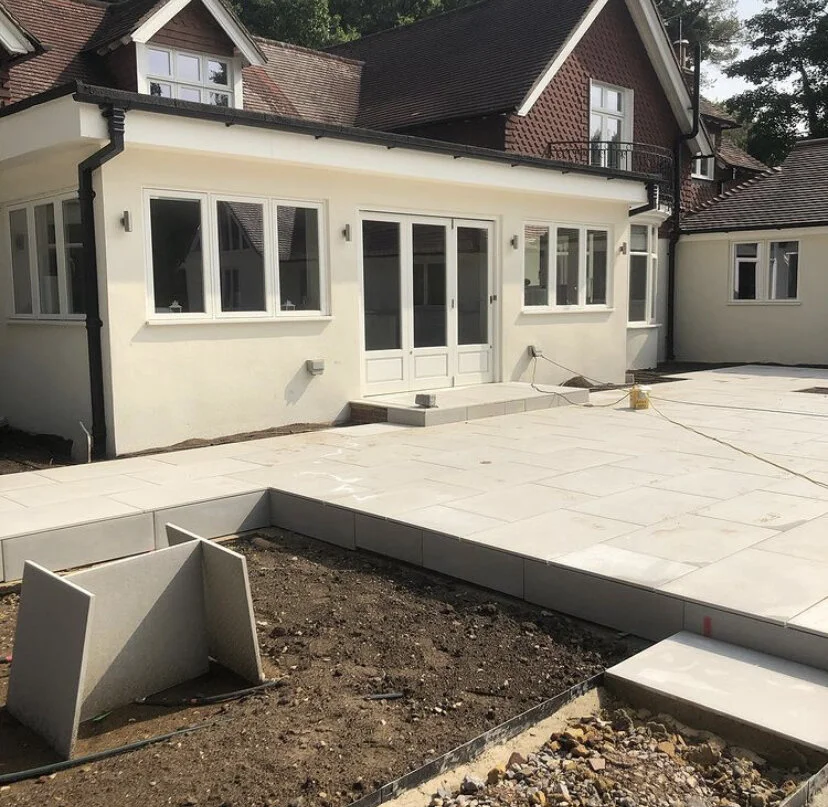 Front porch area of a house under construction, with newly laid concrete paving and construction tools visible.
