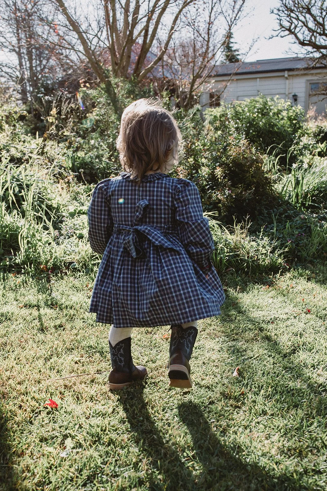 The back of a hand-smocked check picnic dress shows a sash tied in a big bow on a toddler.