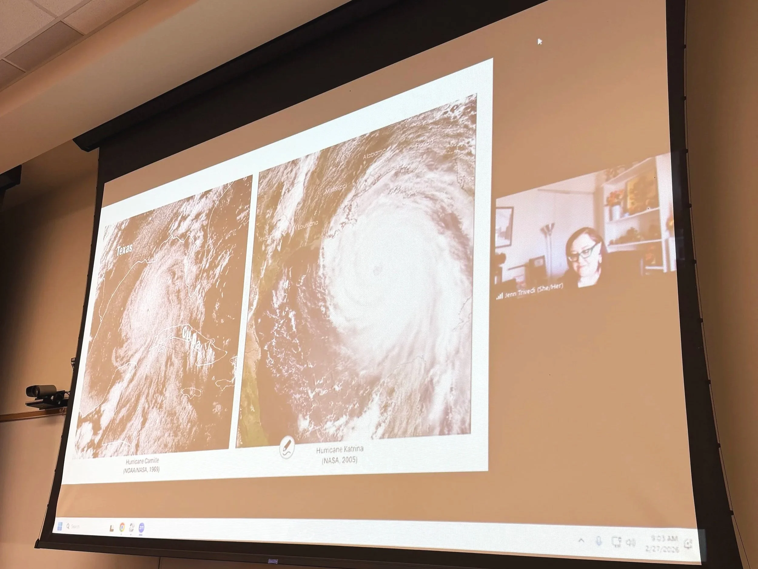 A projector screen showing a Zoom shared screen with 2 satellite images of hurricanes and a woman with purple hair and green glasses speaking.