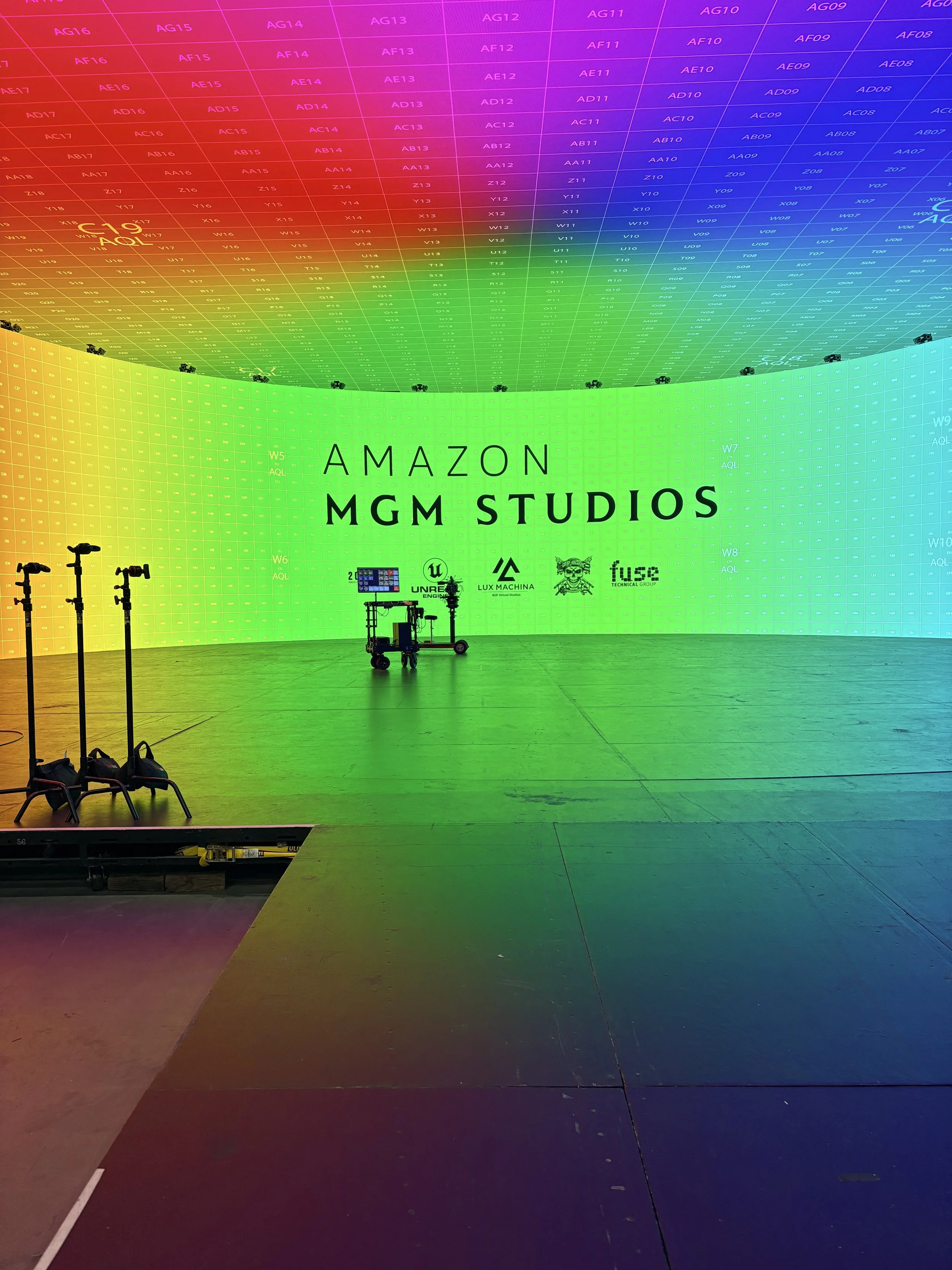 A large colorful digital display with a gradient rainbow spectrum, showing various alphanumeric codes, and the words 'Amazon MGM Studios' in the center.
