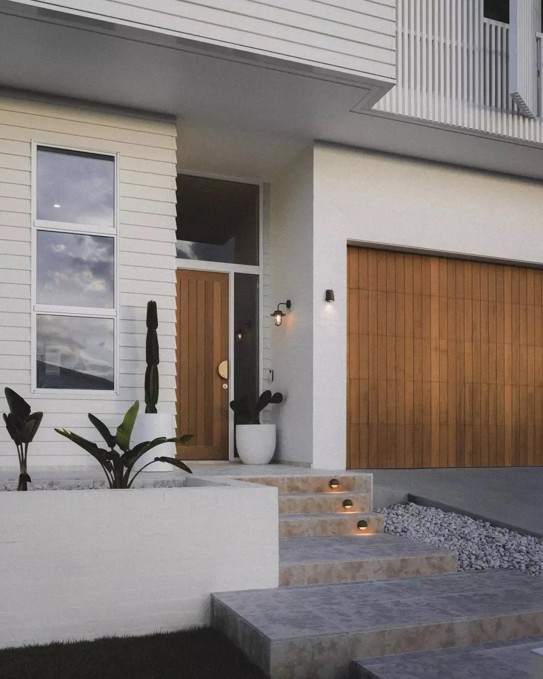 EXTERIOR ACCENTS &bull; The GH Residence exterior facade blends coastal serenity with Mediterranean allure. Featuring pristine white weatherboard panelling, vertical privacy screening, and a timeless travertine porch with brass accents, this design e