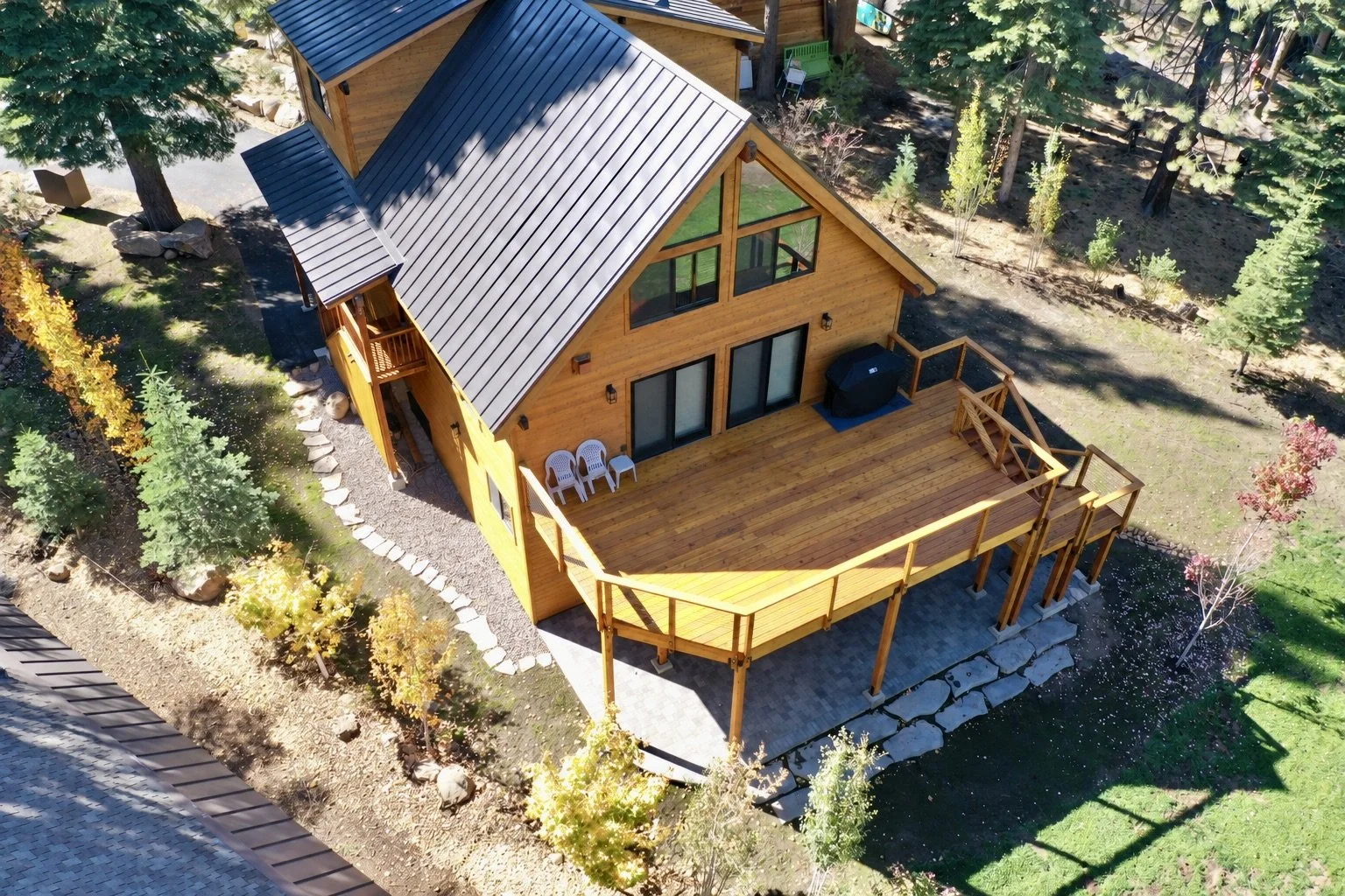 An aerial view of a wooden house with a large deck, surrounded by trees and landscaping.