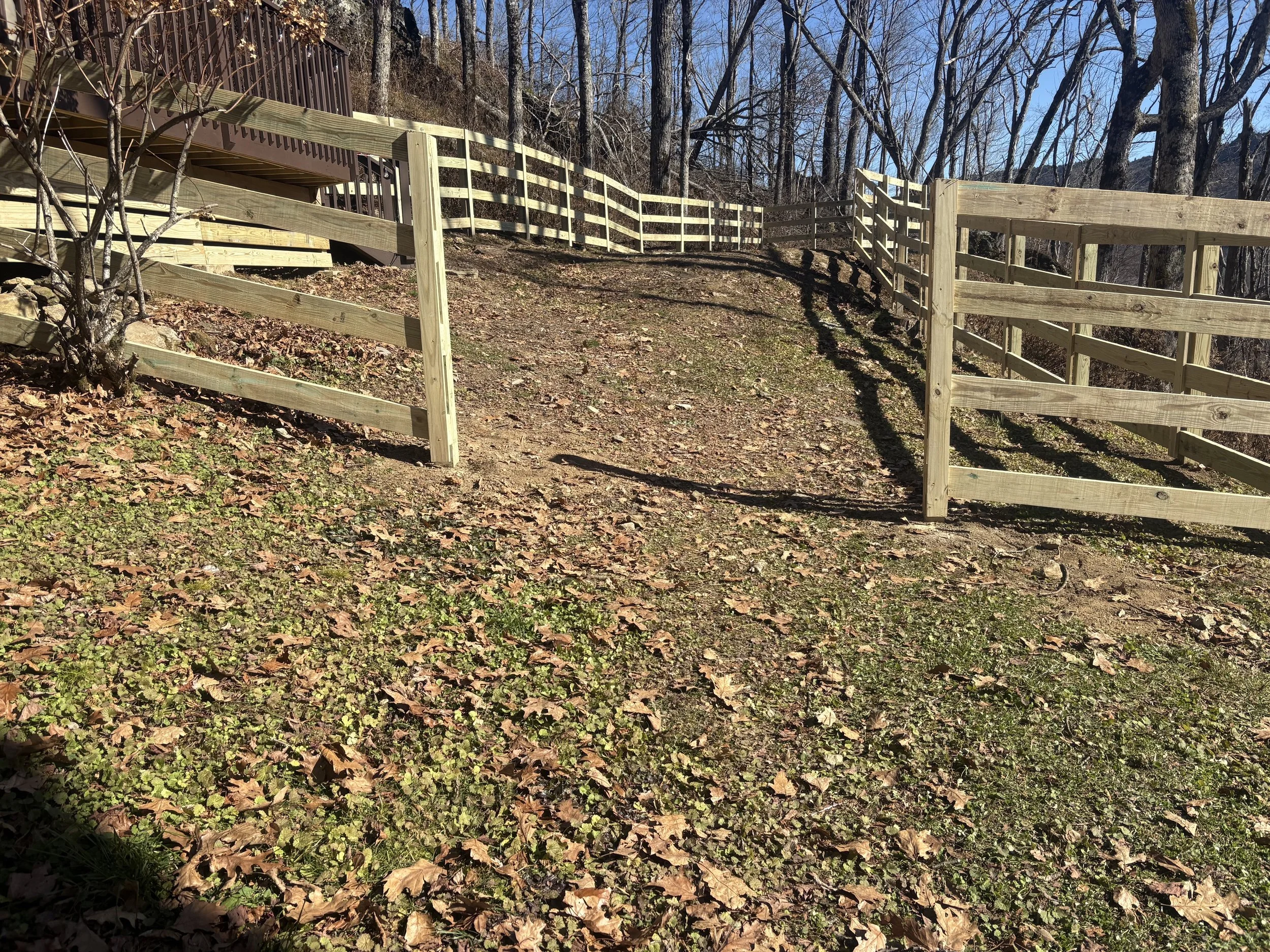 Wooden fencing along a sloped area with leafless trees in the background, on a clear sunny day.